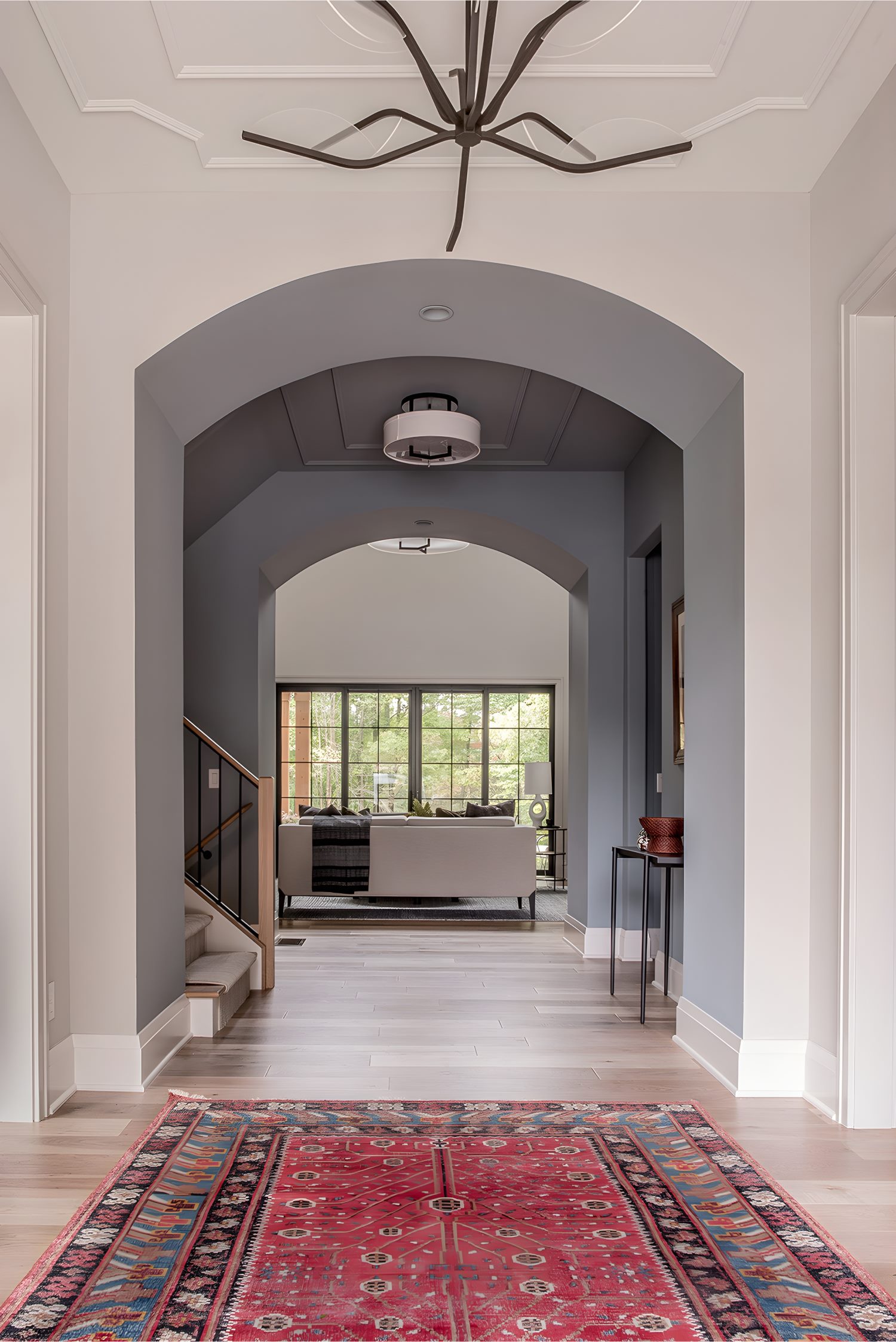 Entryway with arched ceilings, modern chandelier, red patterned rug, and view toward bright living room