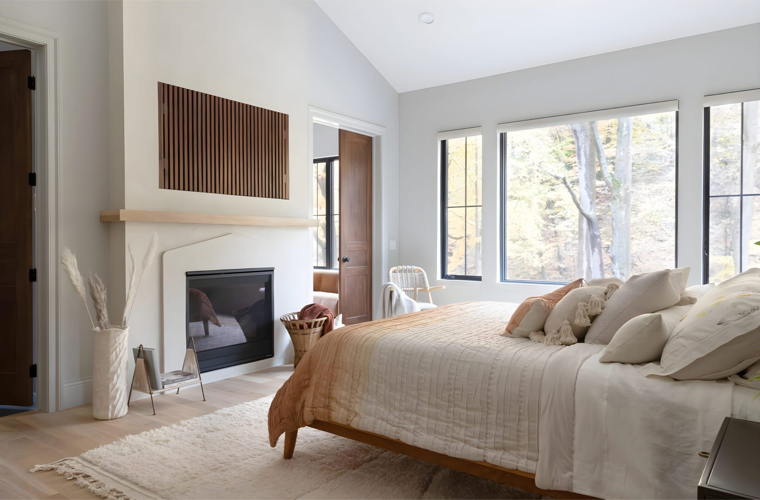 Cozy master bedroom with fireplace, white walls, natural wood bed, layered pillows, and large windows with scenic view