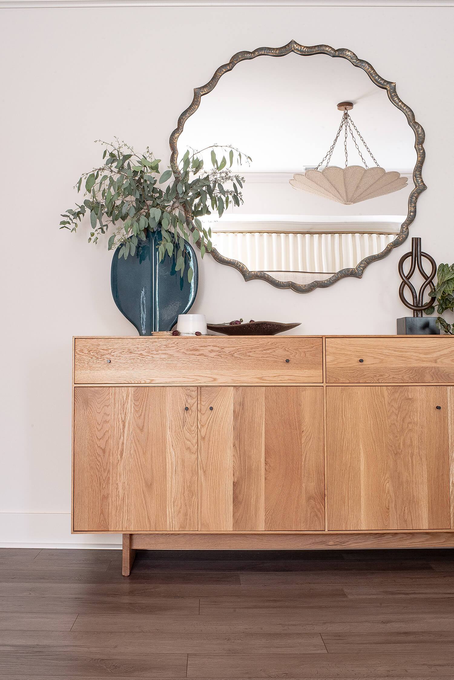 Wooden sideboard with decor accents and large round mirror above, styled with plants and modern accessories on the wall.