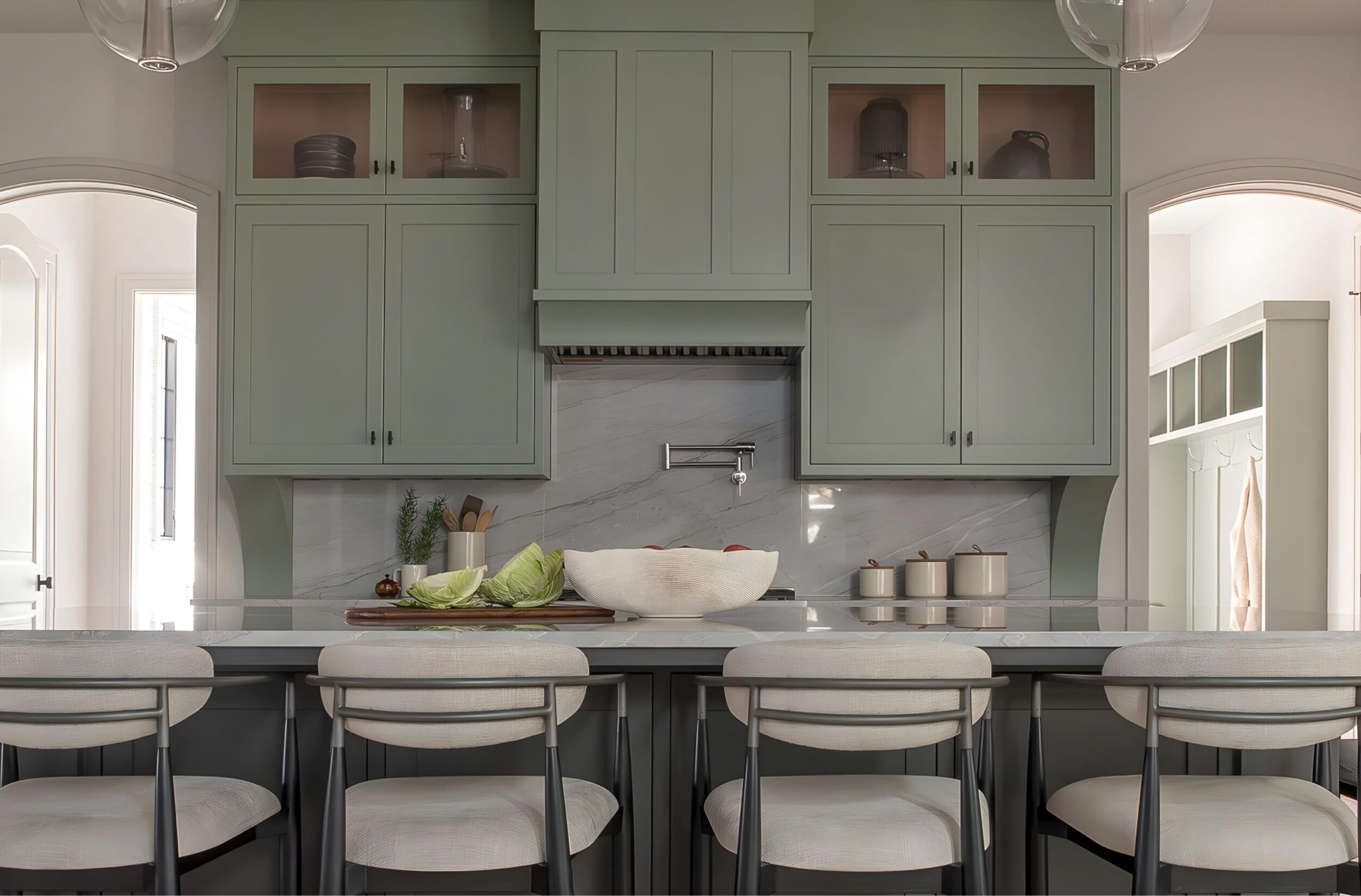 Modern kitchen with sage green cabinets, marble backsplash, and barstools around large island