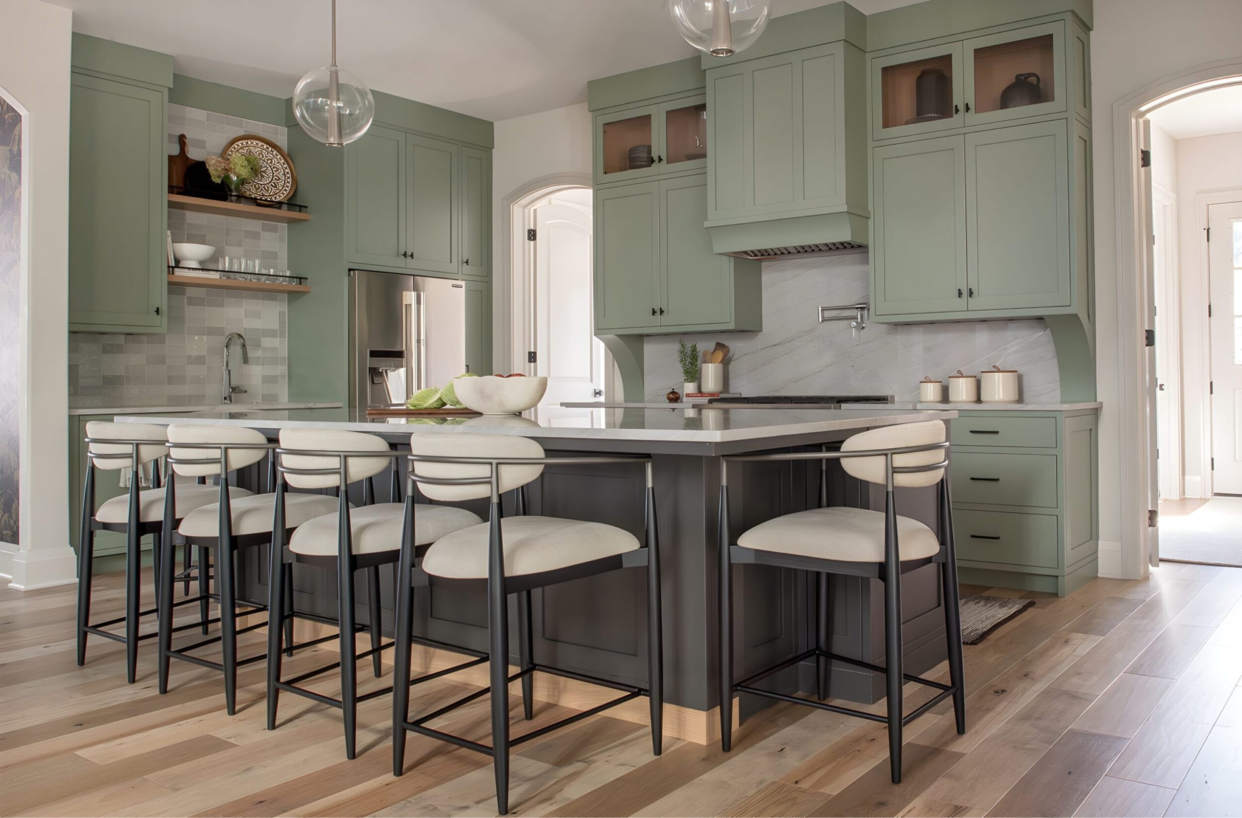 Kitchen island with sage green cabinetry and modern bar stools