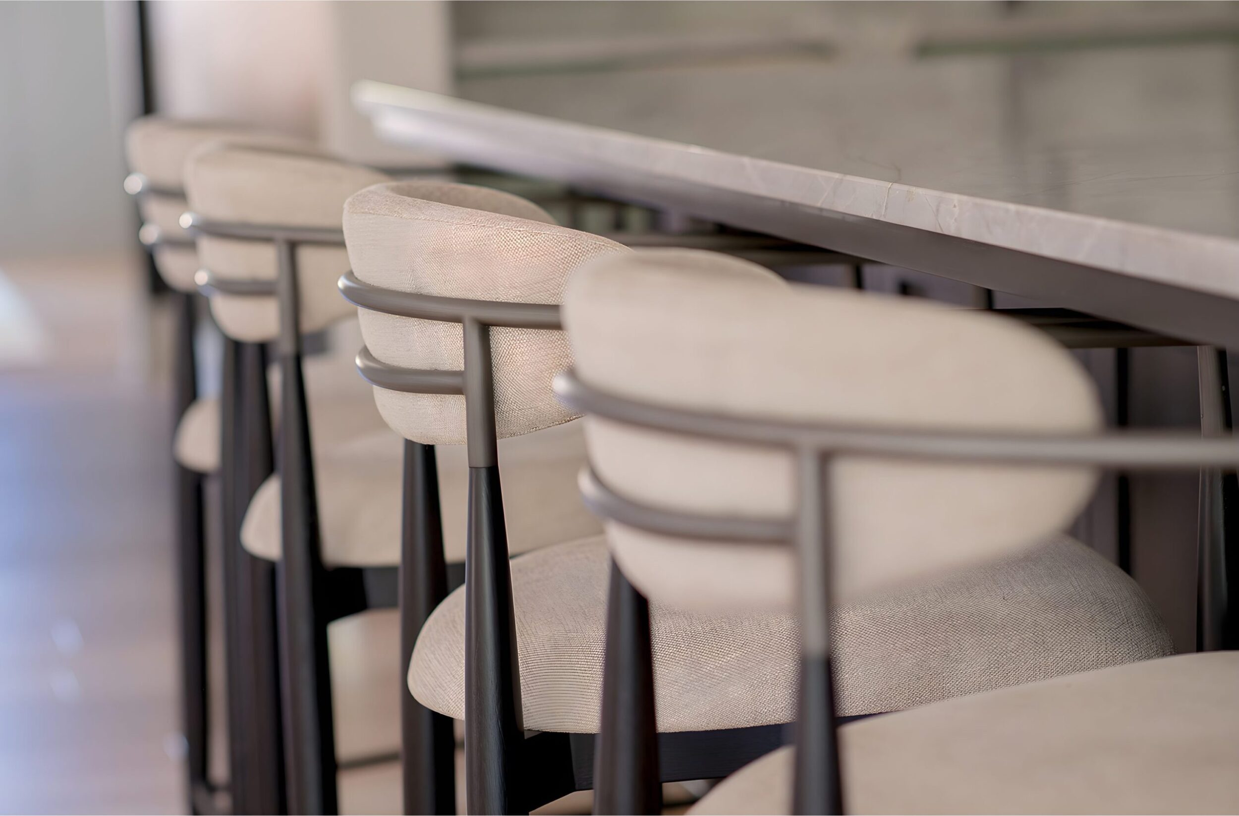 Row of modern upholstered bar stools with sleek metal frames lined up along marble countertop in contemporary kitchen.
