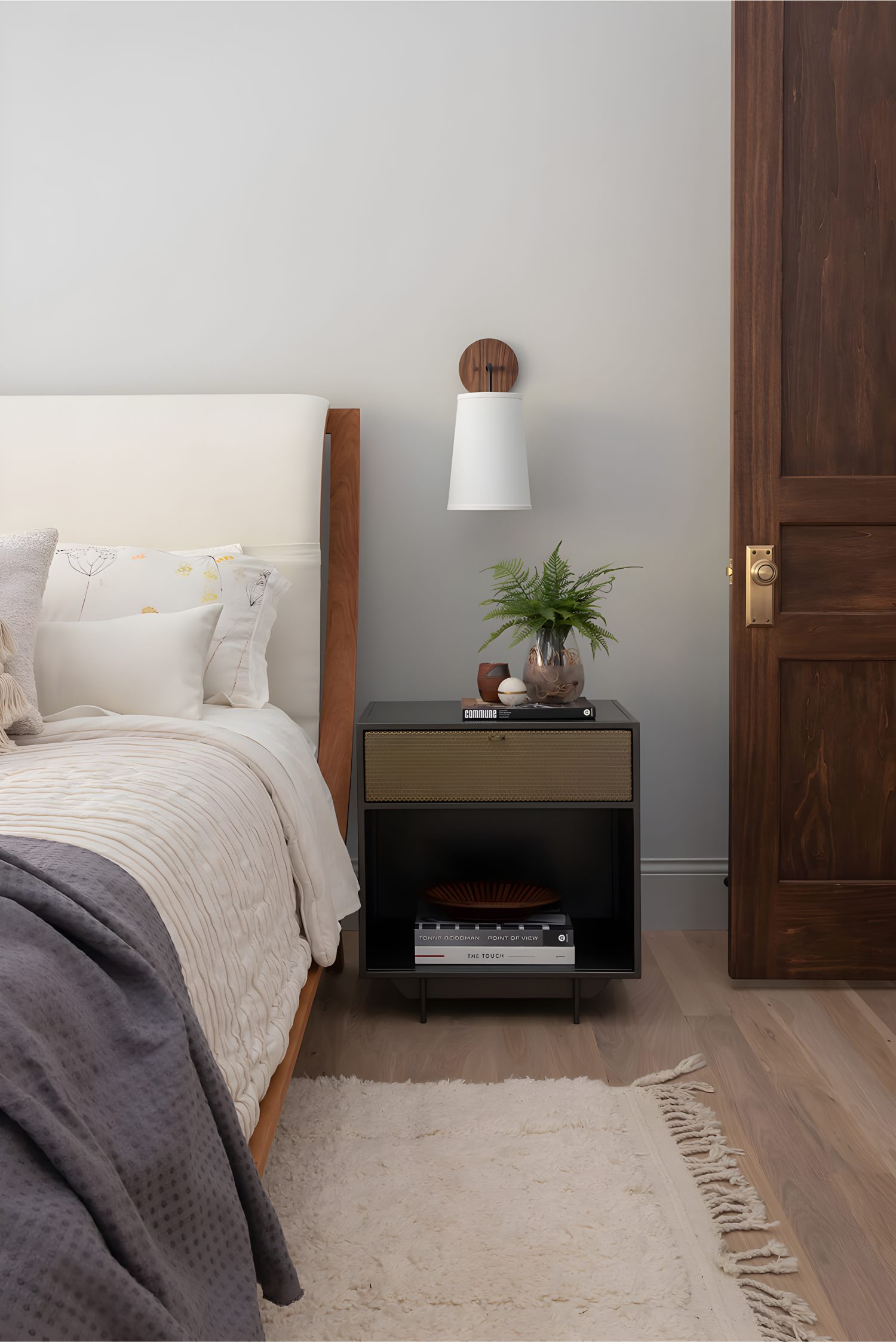 Cozy master bedroom with neutral bedding, wooden bedframe, wall sconce, and black side table styled with books and plants