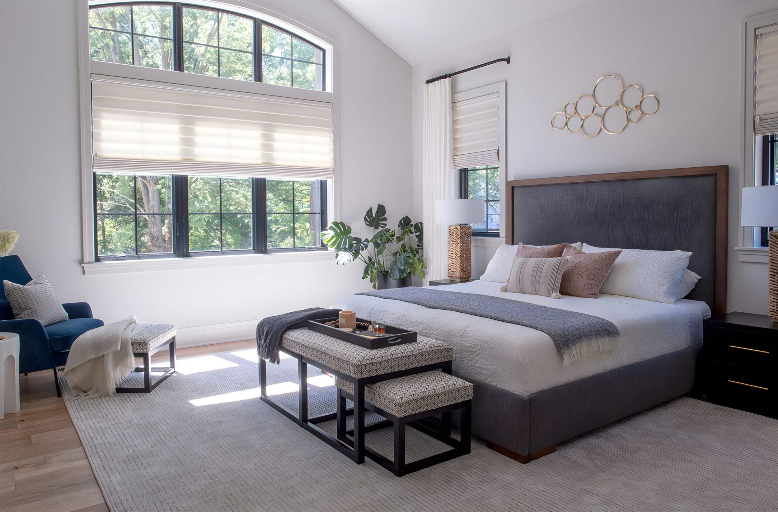 Modern bedroom with large windows, upholstered bed, layered pillows, bench seating, and natural light filling the space