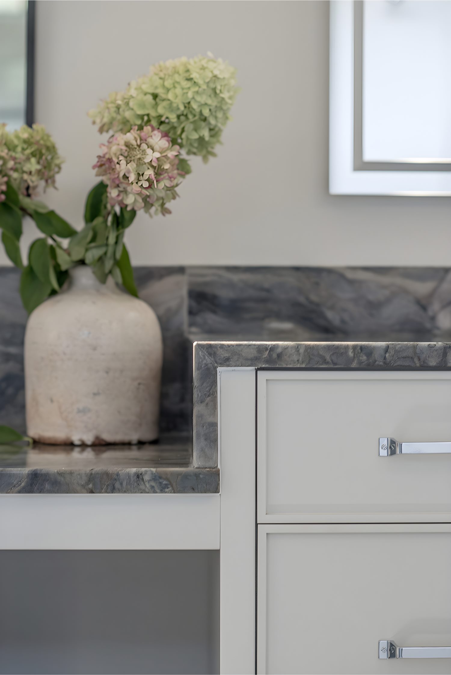 Close-up of elegant bathroom vanity corner with marble countertop, ceramic vase, and fresh hydrangeas in soft light.