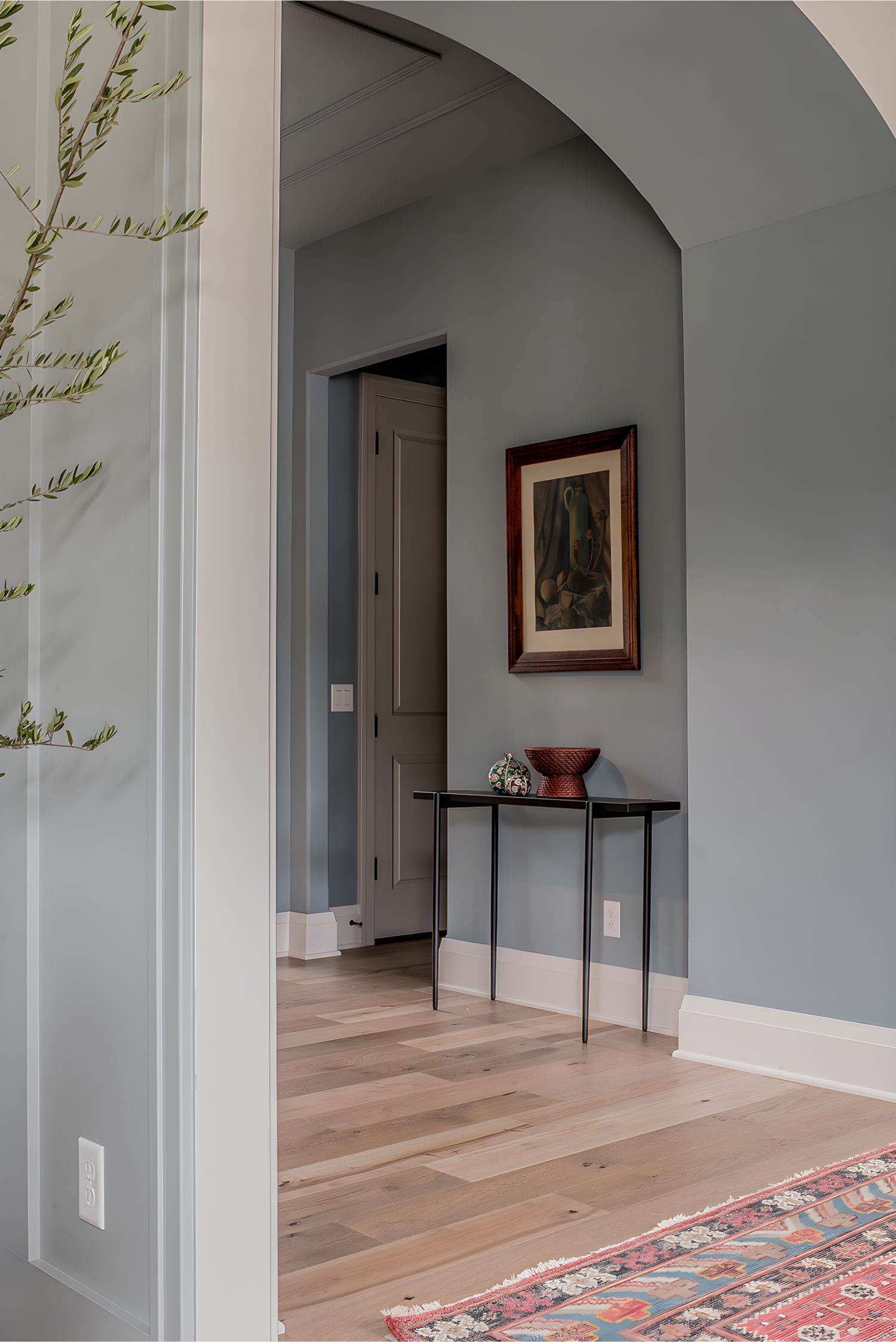 Hallway with arch doorway, light wood floors, narrow black console table, framed art, and decorative bowl