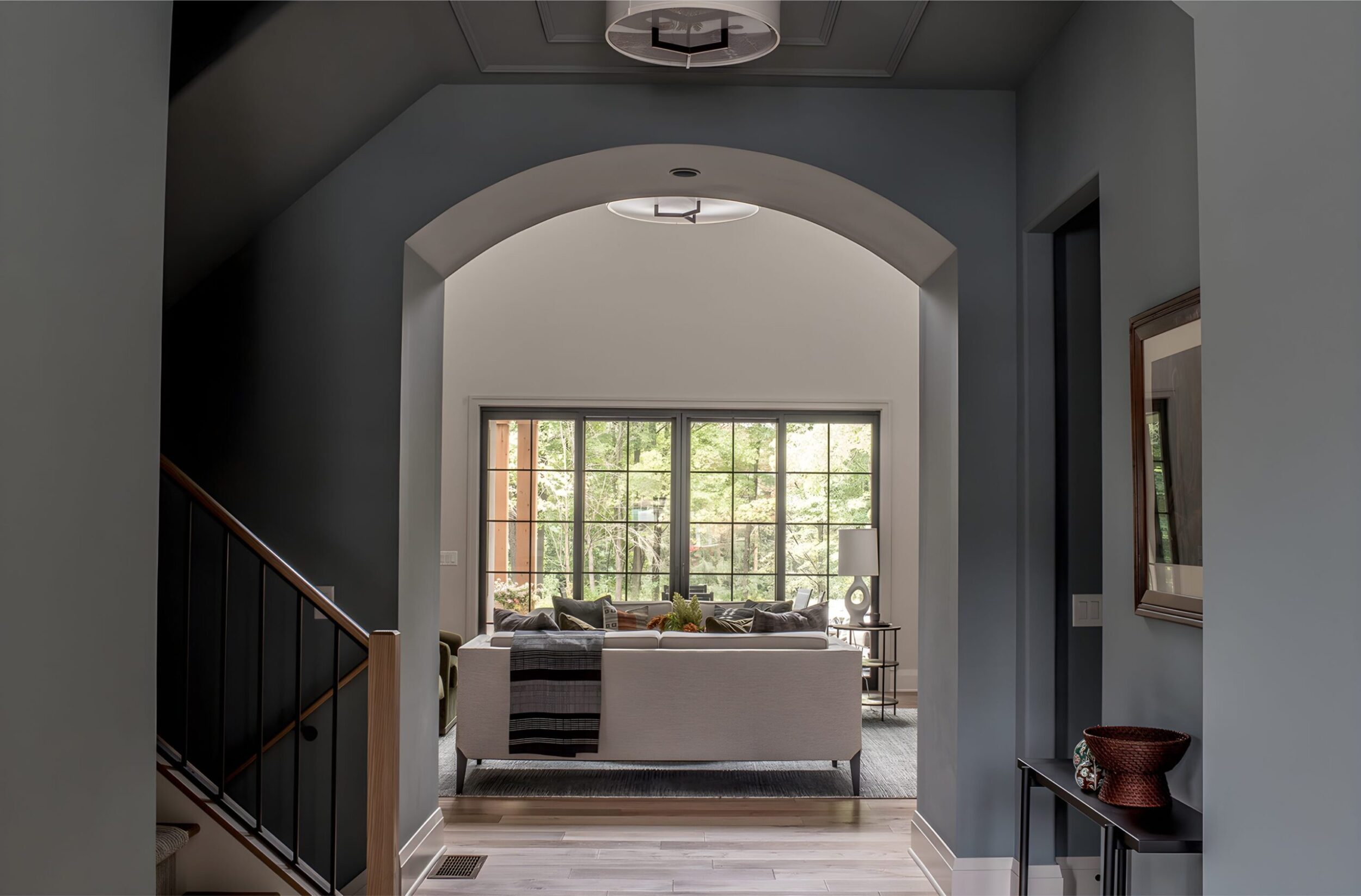 Elegant hallway view with arched opening leading to bright living room, featuring large windows and modern sofa.