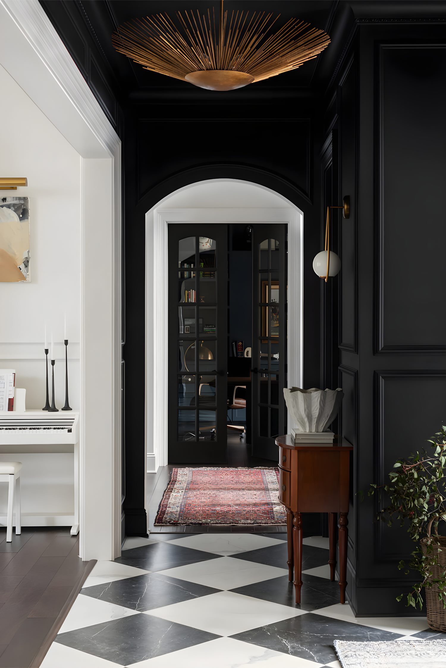 Black and white checkered floor hallway with black walls, gold sunburst ceiling light, and French glass doors