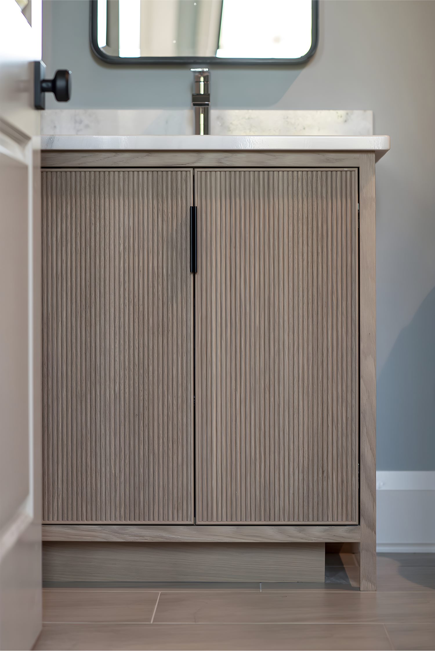 Modern bathroom vanity with ribbed wood cabinet doors, marble countertop, and sleek matte black faucet