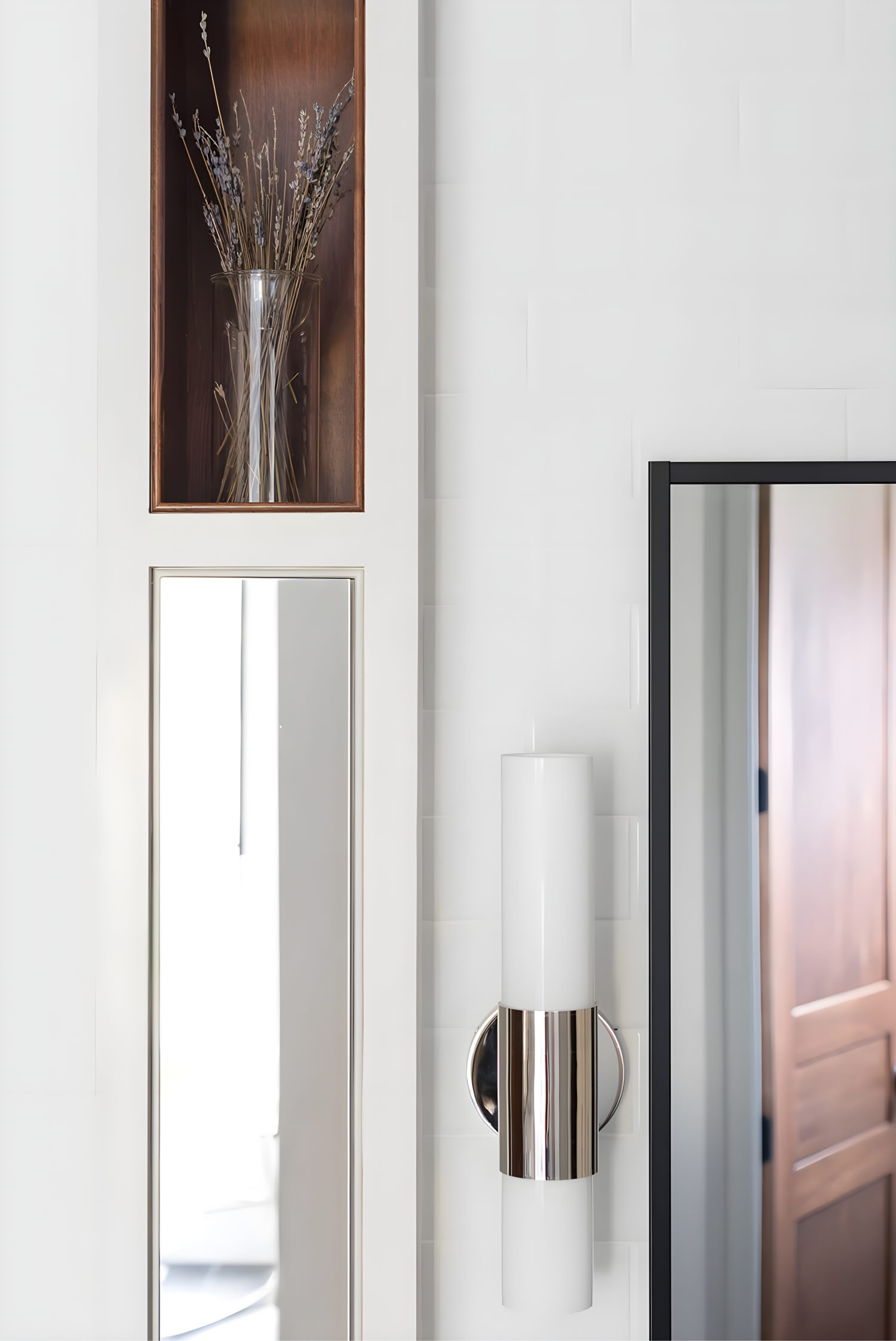 Spacious bathroom featuring white cabinetry, wide mirror, and elegant decor with fresh flowers and gold accents.