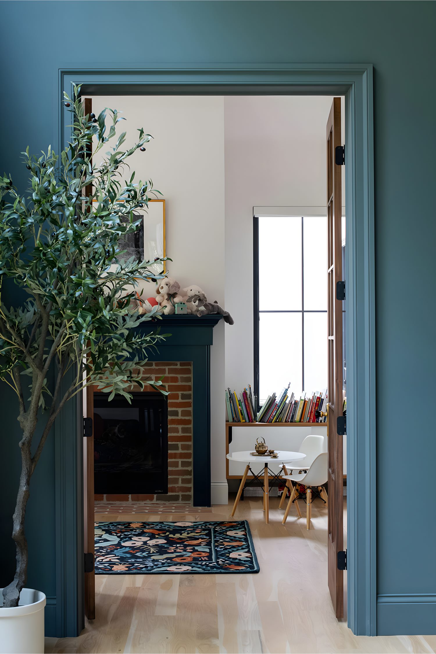 Doorway view of children’s room with brick fireplace, stuffed animals, books, and patterned rug.