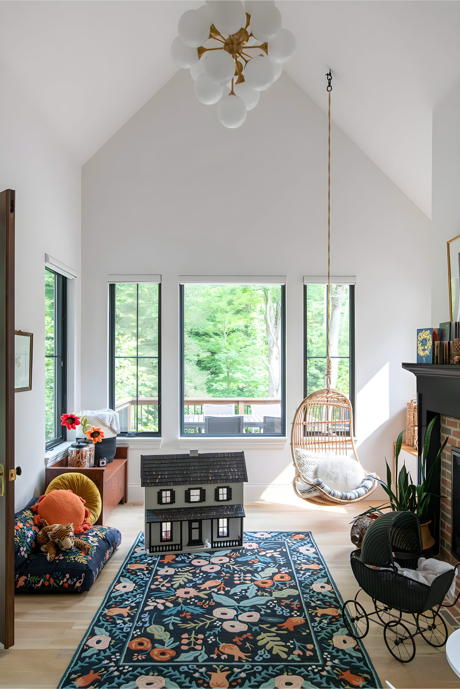 Playroom with colorful floral rug, dollhouse, rattan hanging chair, and modern chandelier under vaulted ceiling.
