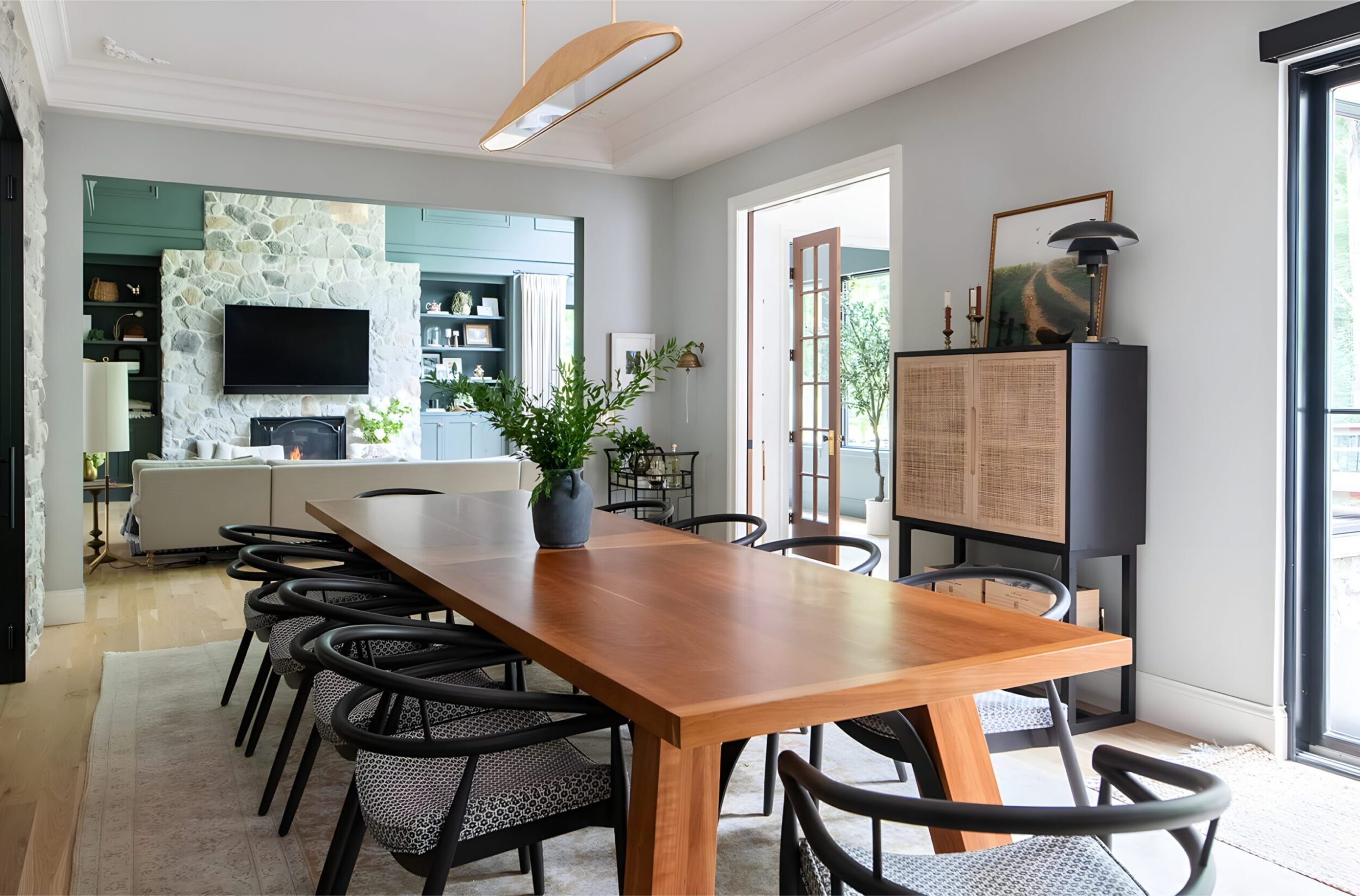 Open dining room with wood table, stone fireplace, modern chandelier, and elegant mix of rustic and sleek decor.