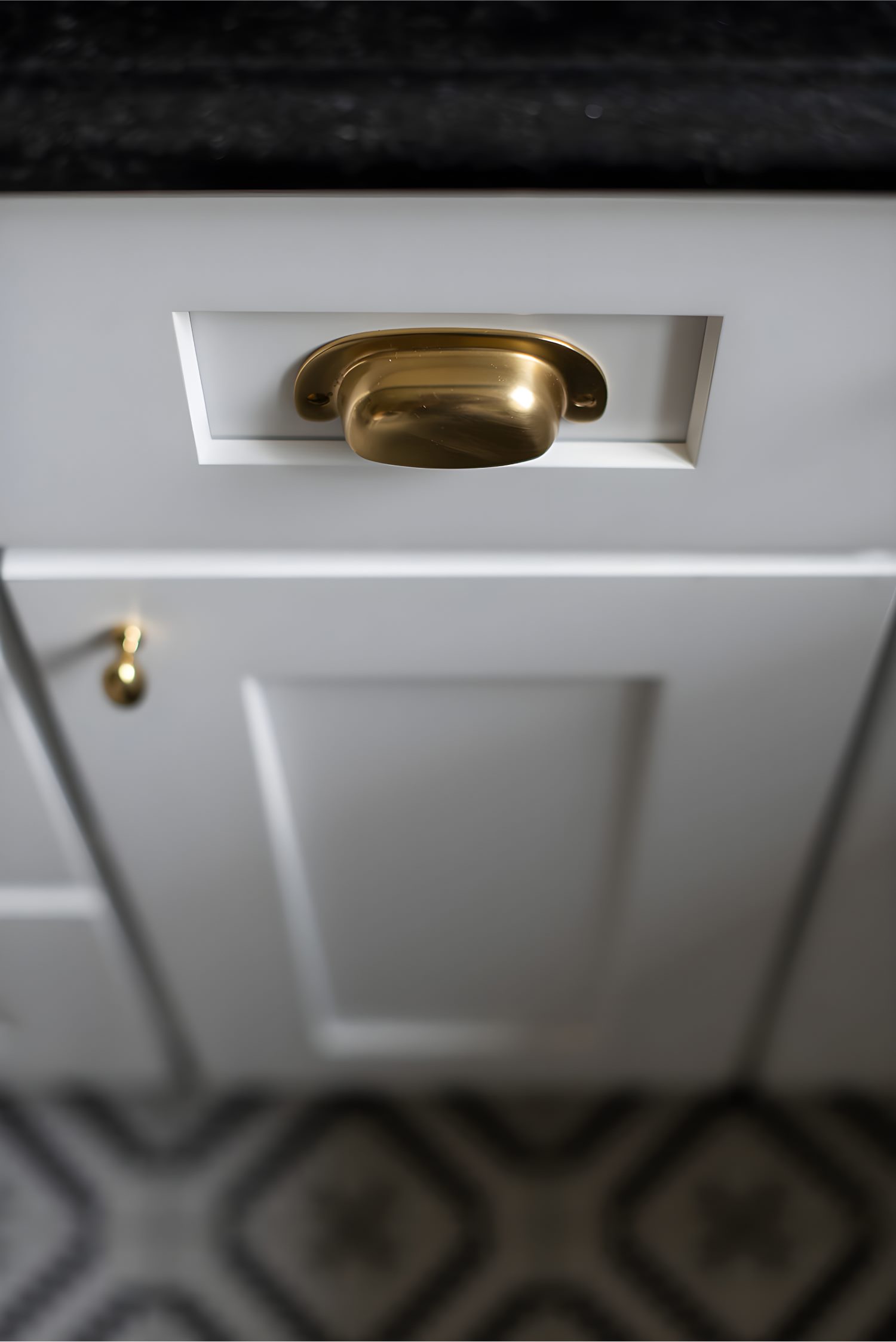 Close-up of white cabinet with gold pull handle and black countertop detail in a modern kitchen.