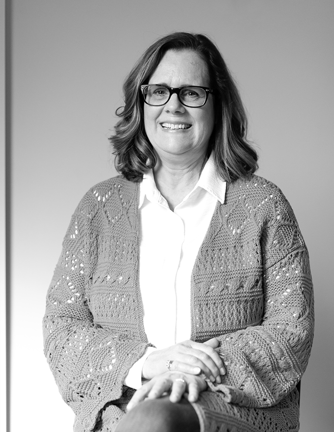Black-and-white portrait of woman with glasses smiling, wearing patterned knit cardigan over collared shirt