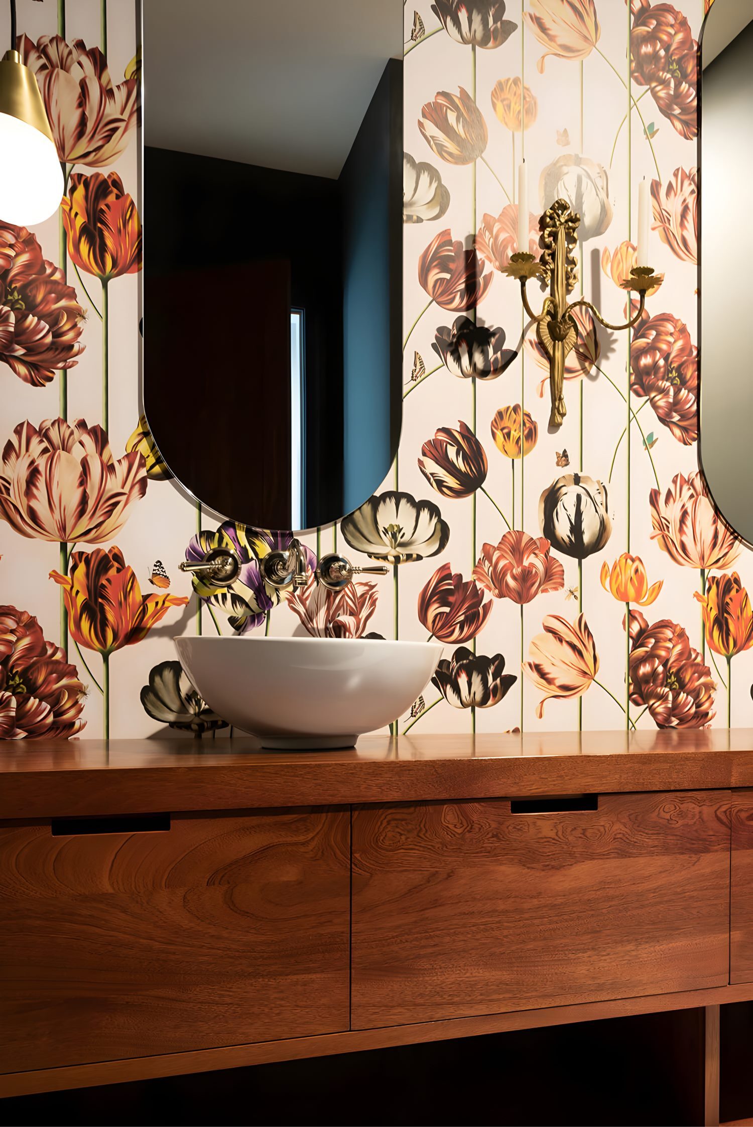 Modern vanity with wood cabinet, white vessel sink, floral tulip wallpaper, brass sconce, and arched mirror accent