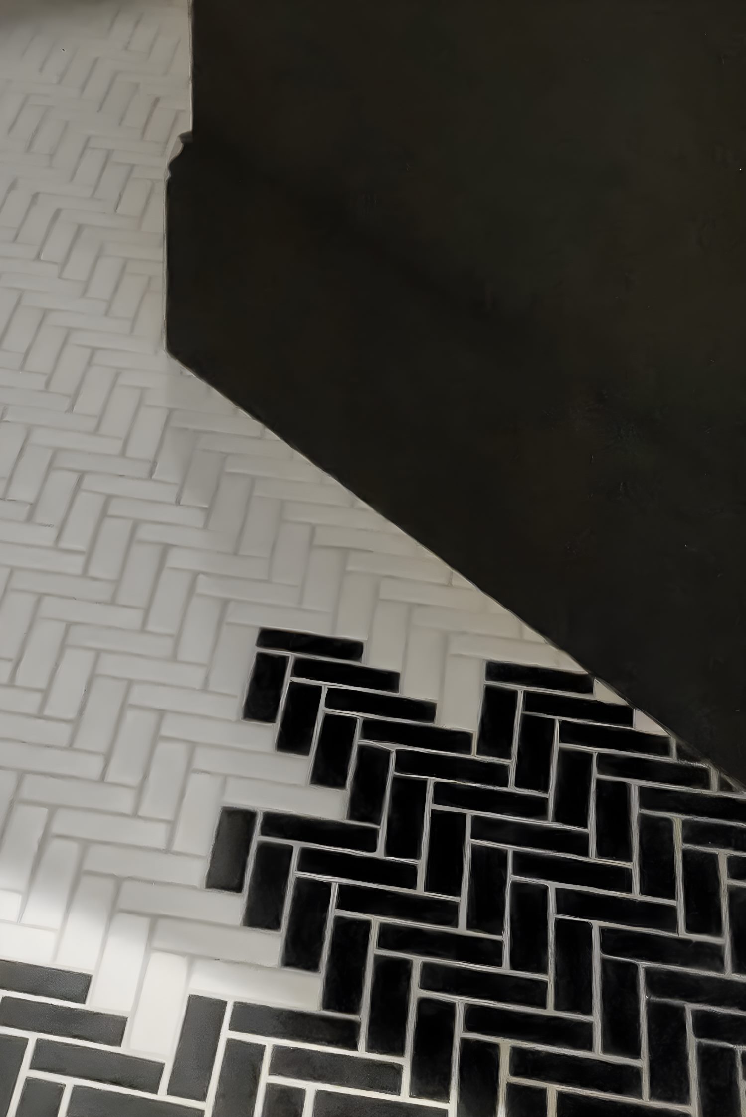Black and white herringbone tile floor with creative gradient design blending two contrasting tones along the wall