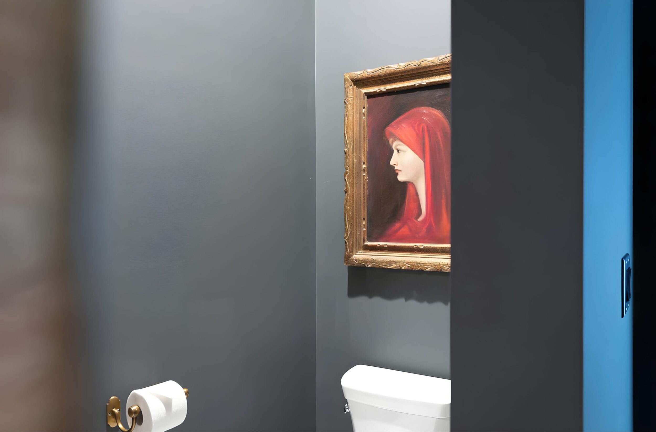 Dark powder bathroom with framed portrait art of woman in red hood above toilet, gold toilet paper holder on gray wall