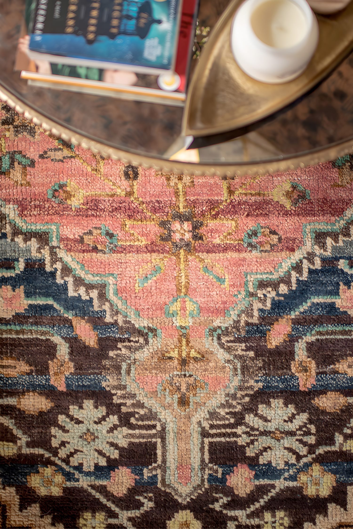 Close-up of vibrant patterned rug in pink, blue, and brown tones with round glass coffee table above.