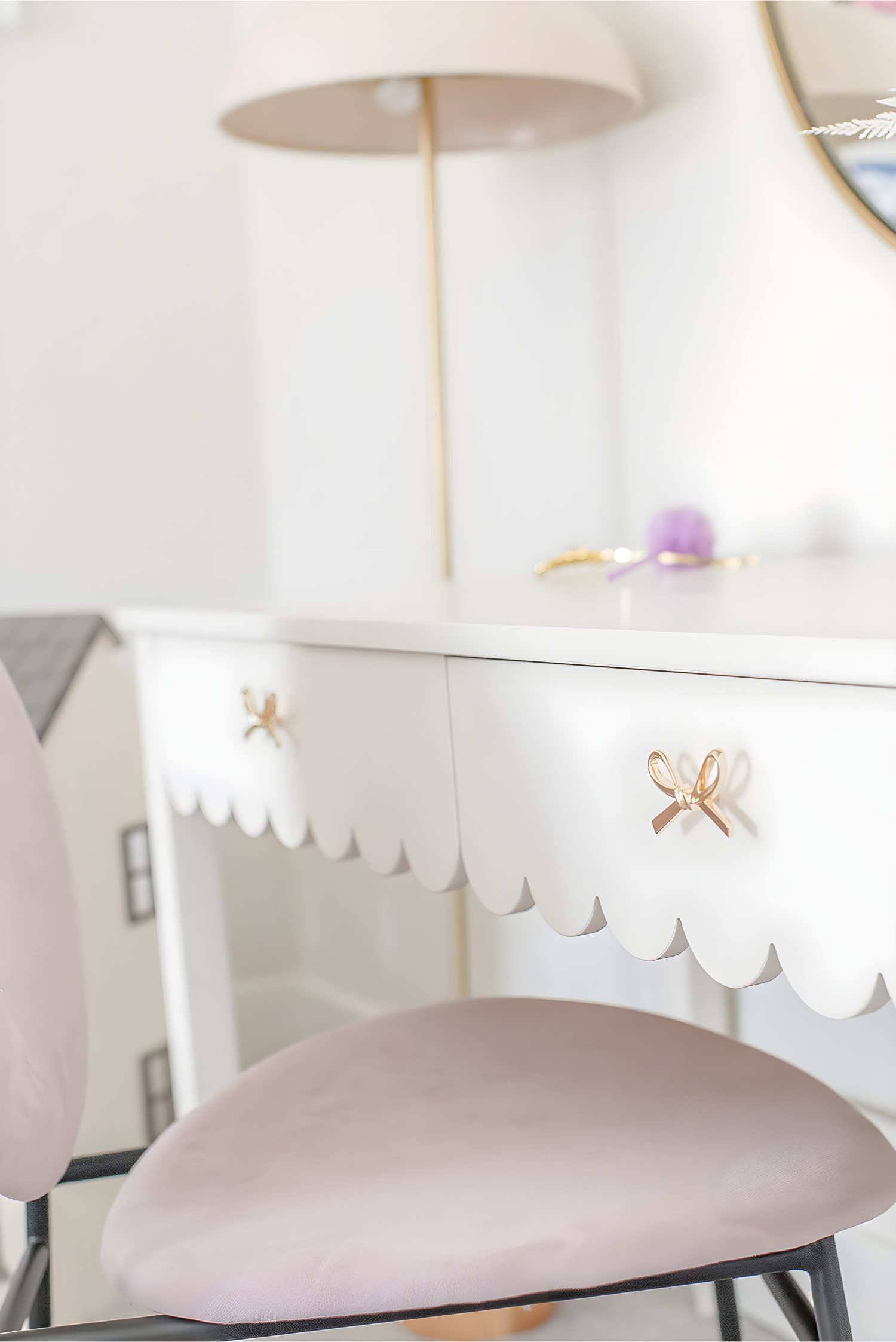 Close-up of white desk with scalloped edge, pink chair, and gold bow drawer pulls in girls’ bedroom