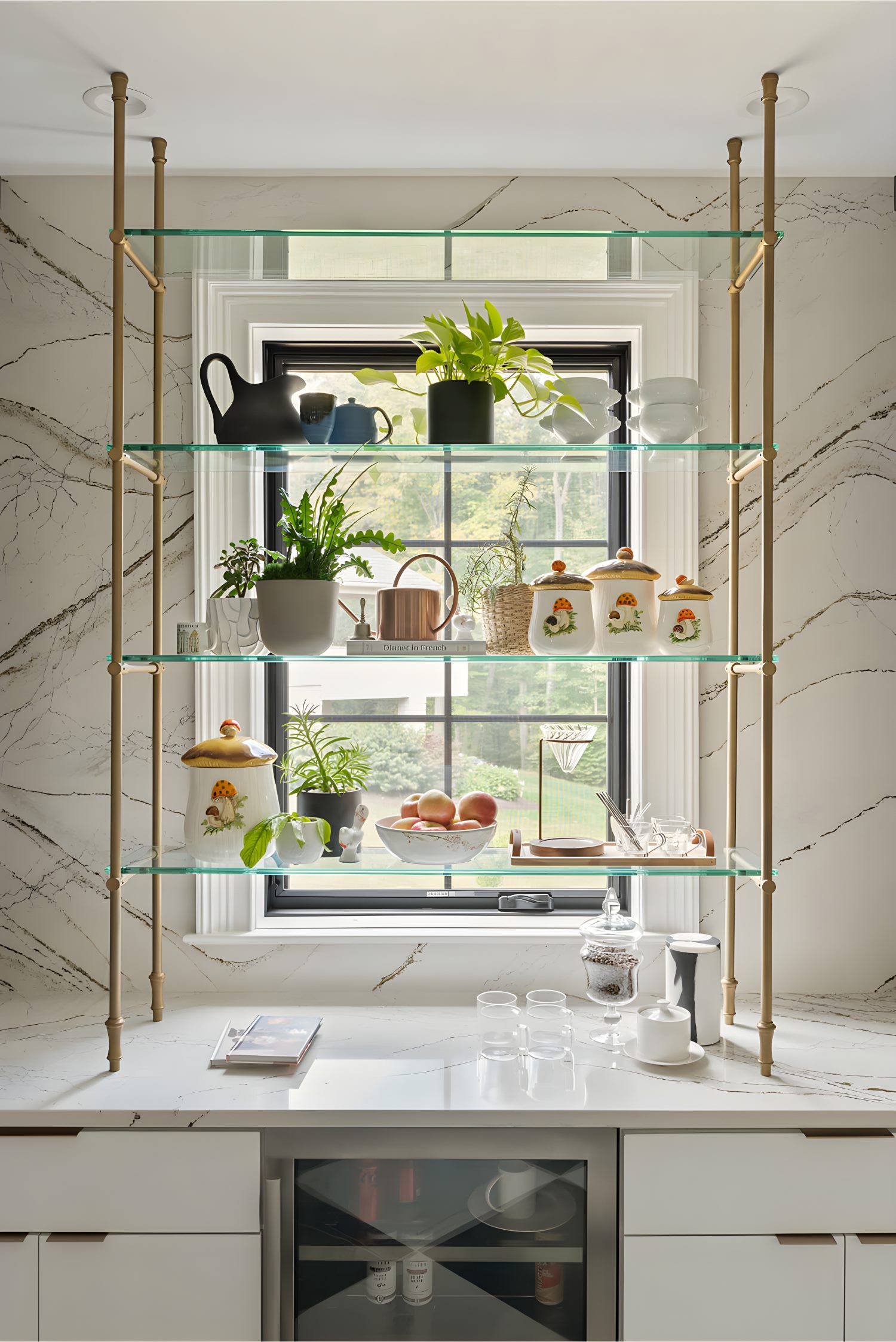 Open shelving with glass shelves, plants, ceramic jars, watering can, apples, and decor against window with marble wall