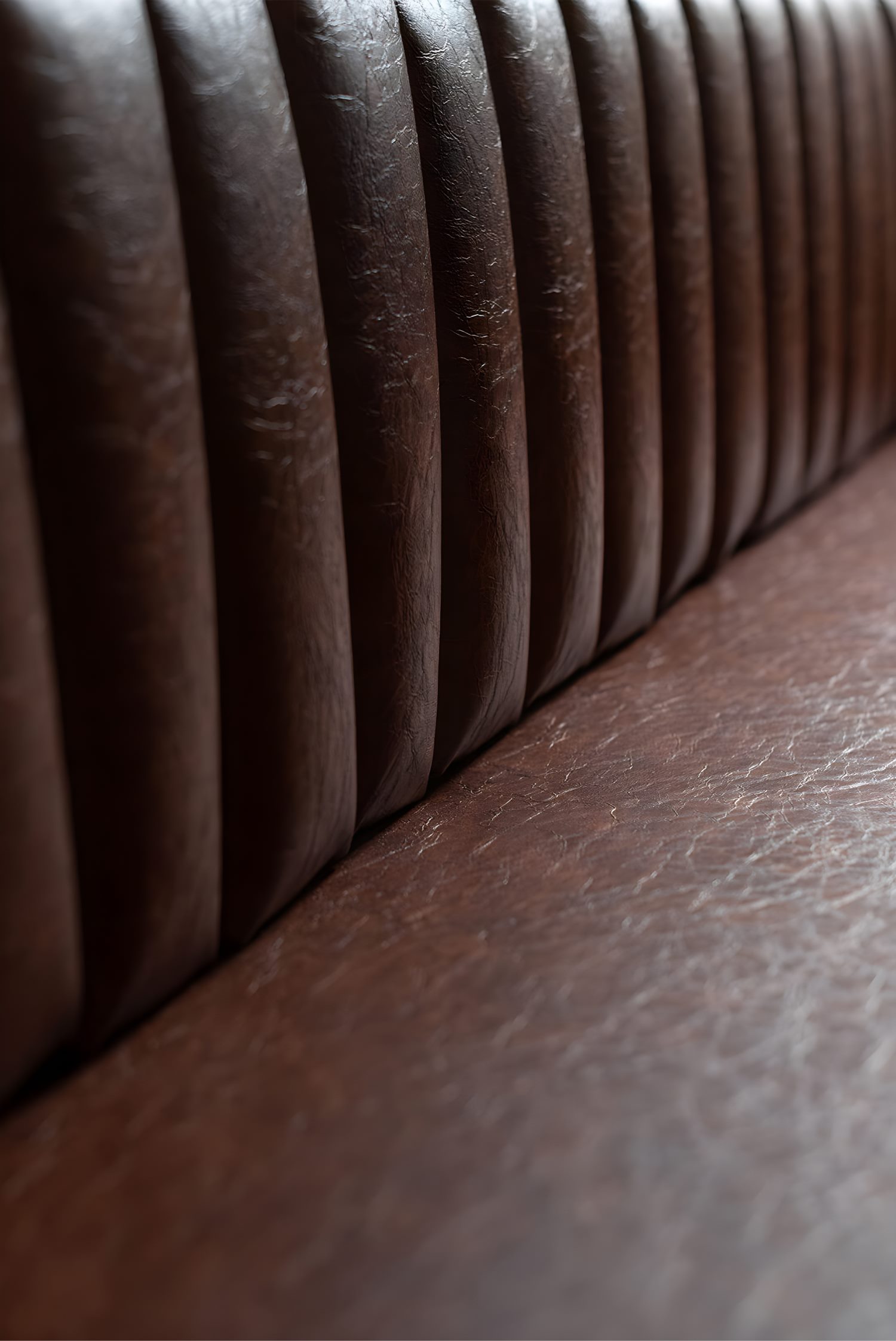 Close-up of brown leather banquette with vertical stitched pattern, highlighting textured grain and natural wear details