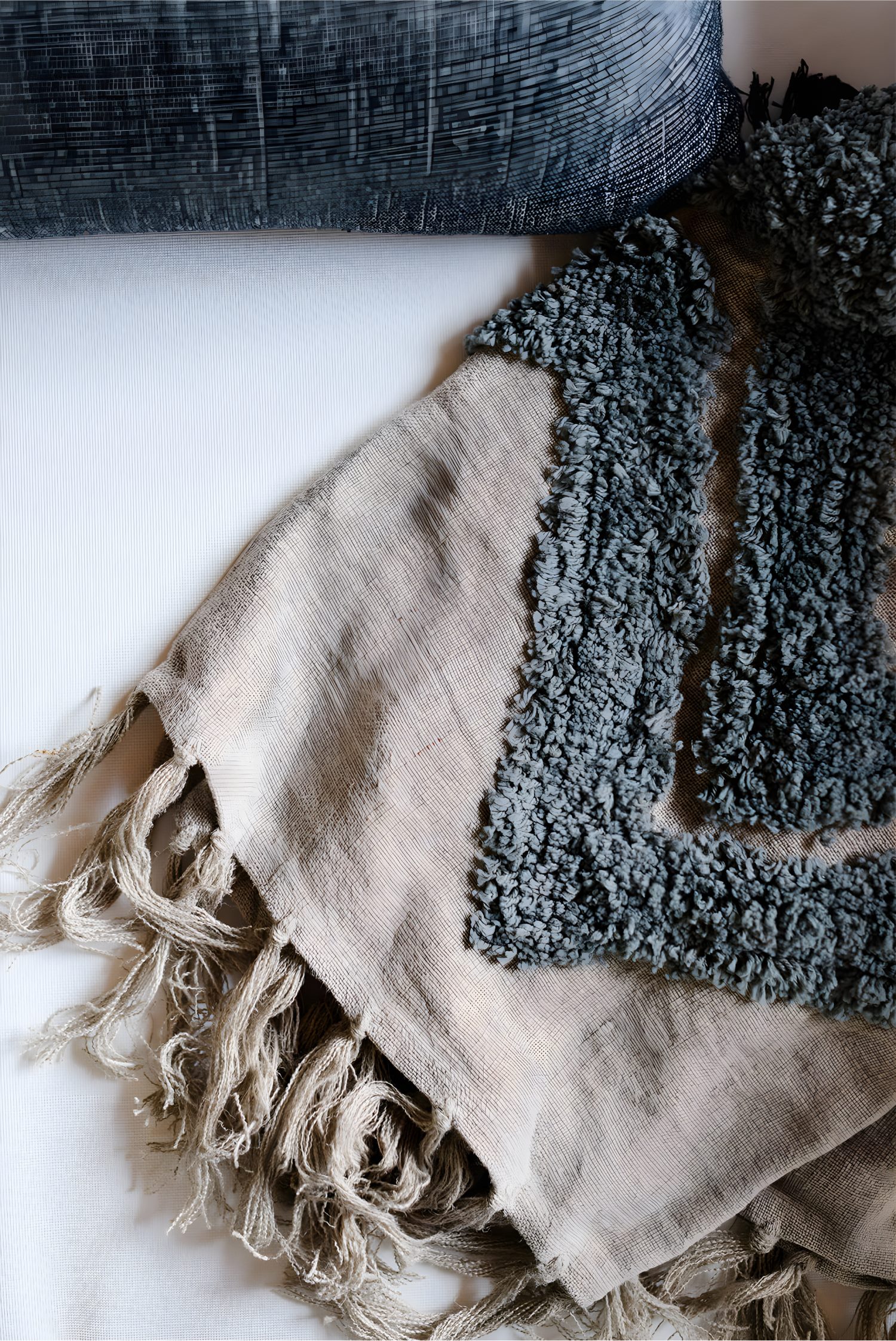 Close-up of textured fabric with beige fringe and blue patterned woven blanket draped over a white surface