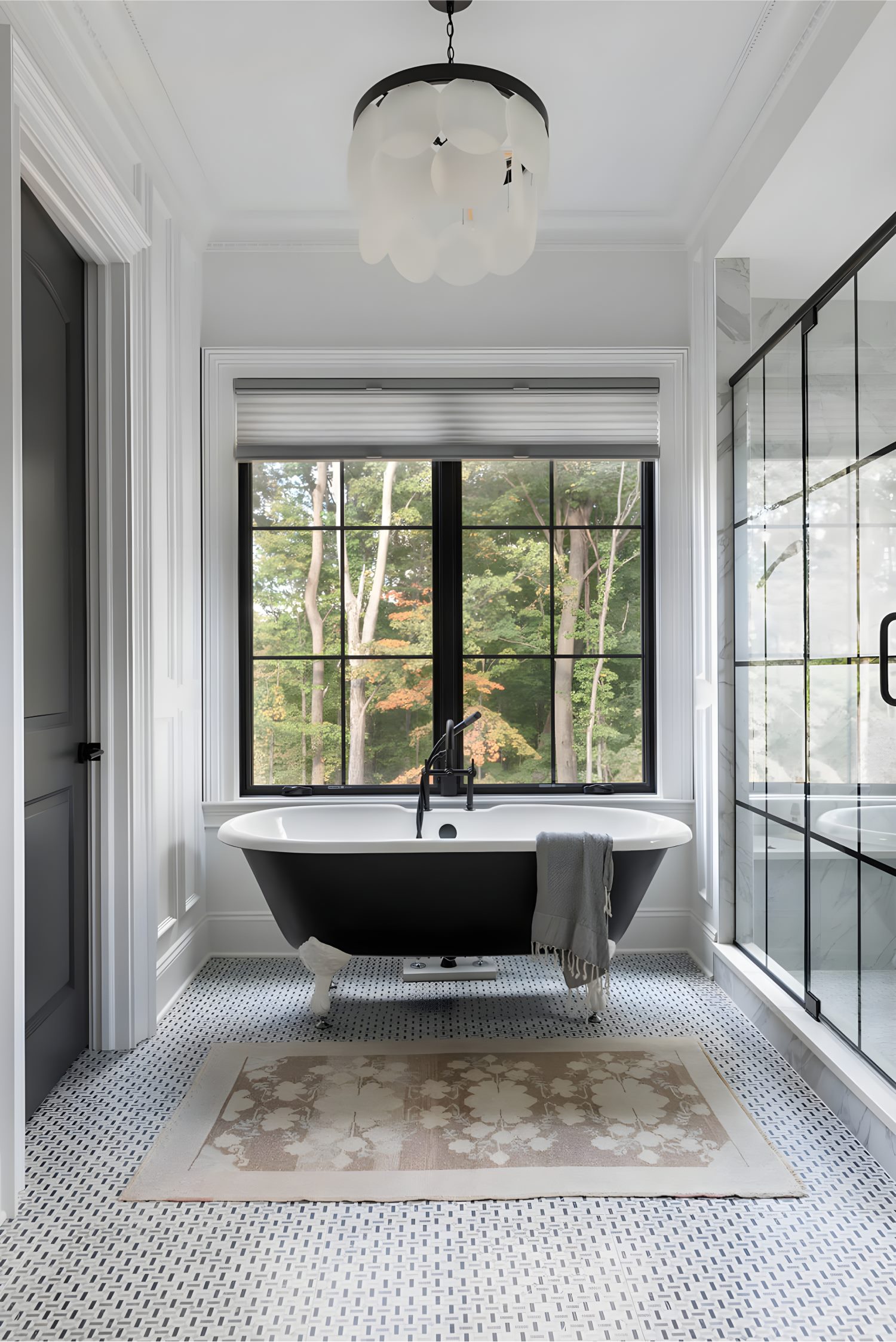 Modern bathroom with black clawfoot tub, large window view of trees, geometric tile floor, and glass shower wall