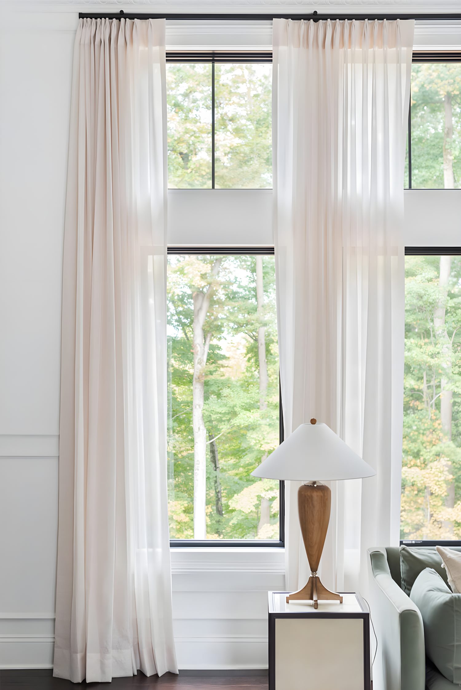 Tall window with sheer white curtains beside modern lamp on side table, soft light highlighting interior textures