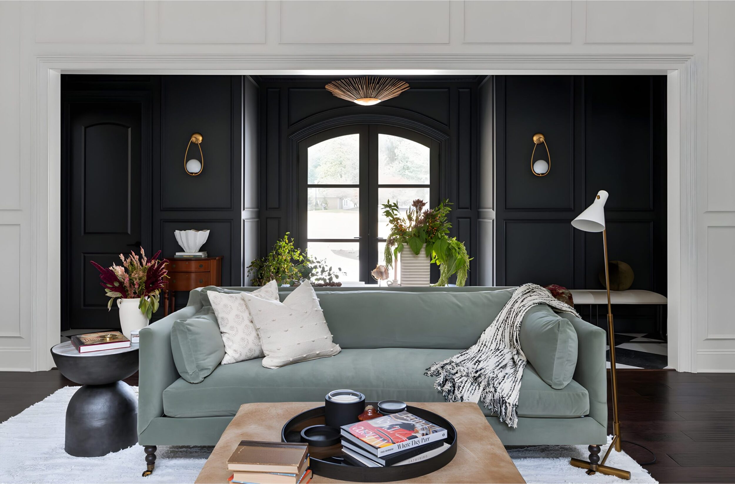 Living room with green sofa, black accent wall, modern lighting, and décor including books, flowers, and lamp
