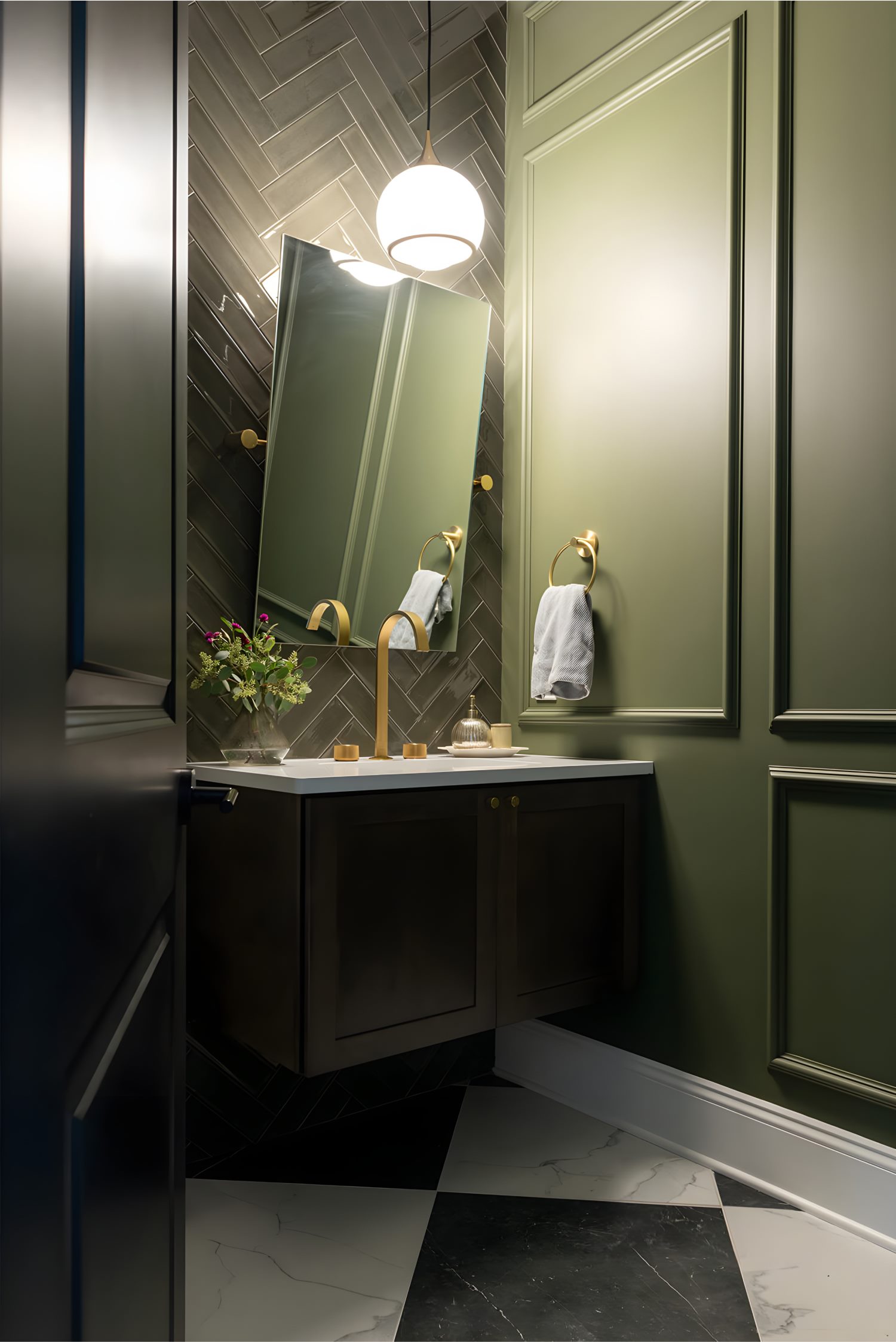 Small bathroom with olive green paneled walls, brass fixtures, floating vanity, and herringbone tile backsplash