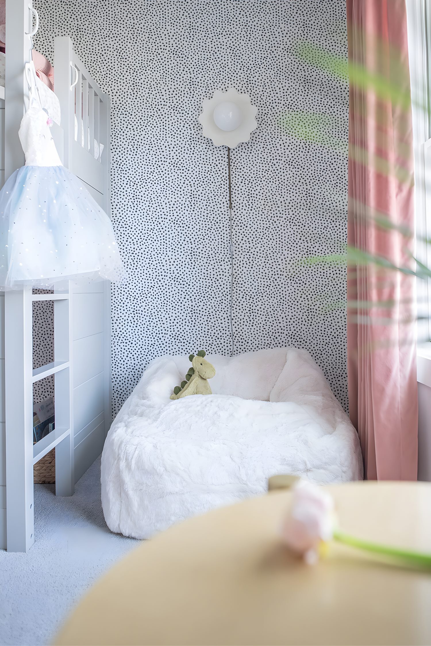 Cozy reading nook in kids’ room with white beanbag, plush dinosaur toy, dotted accent wall, and pink curtains