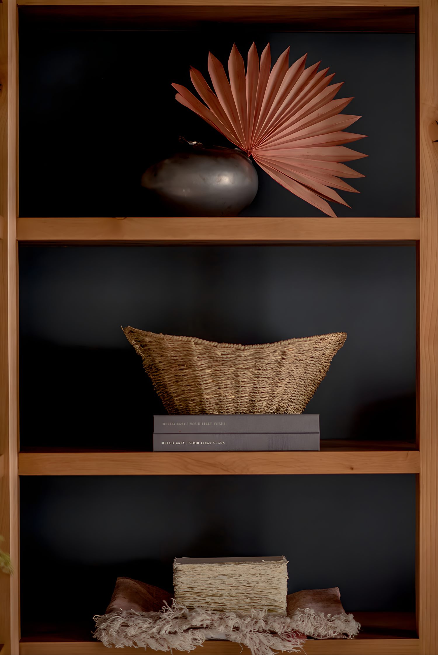 Wooden shelf with decorative objects including ceramic vase, woven basket, books, and dried palm leaf accent.
