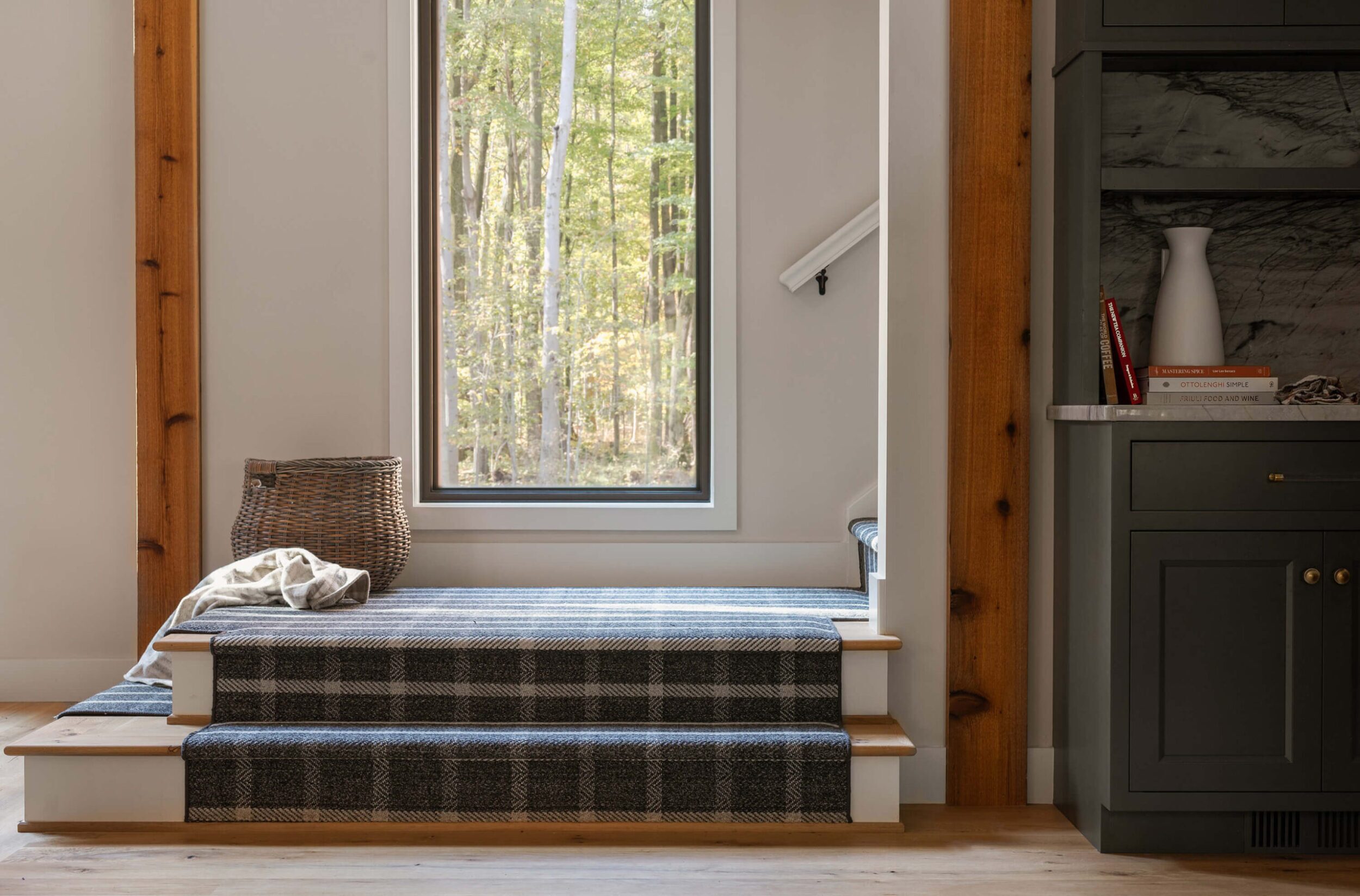 Stair landing with plaid carpet, large window view of trees, wicker basket, and modern built-in cabinetry.