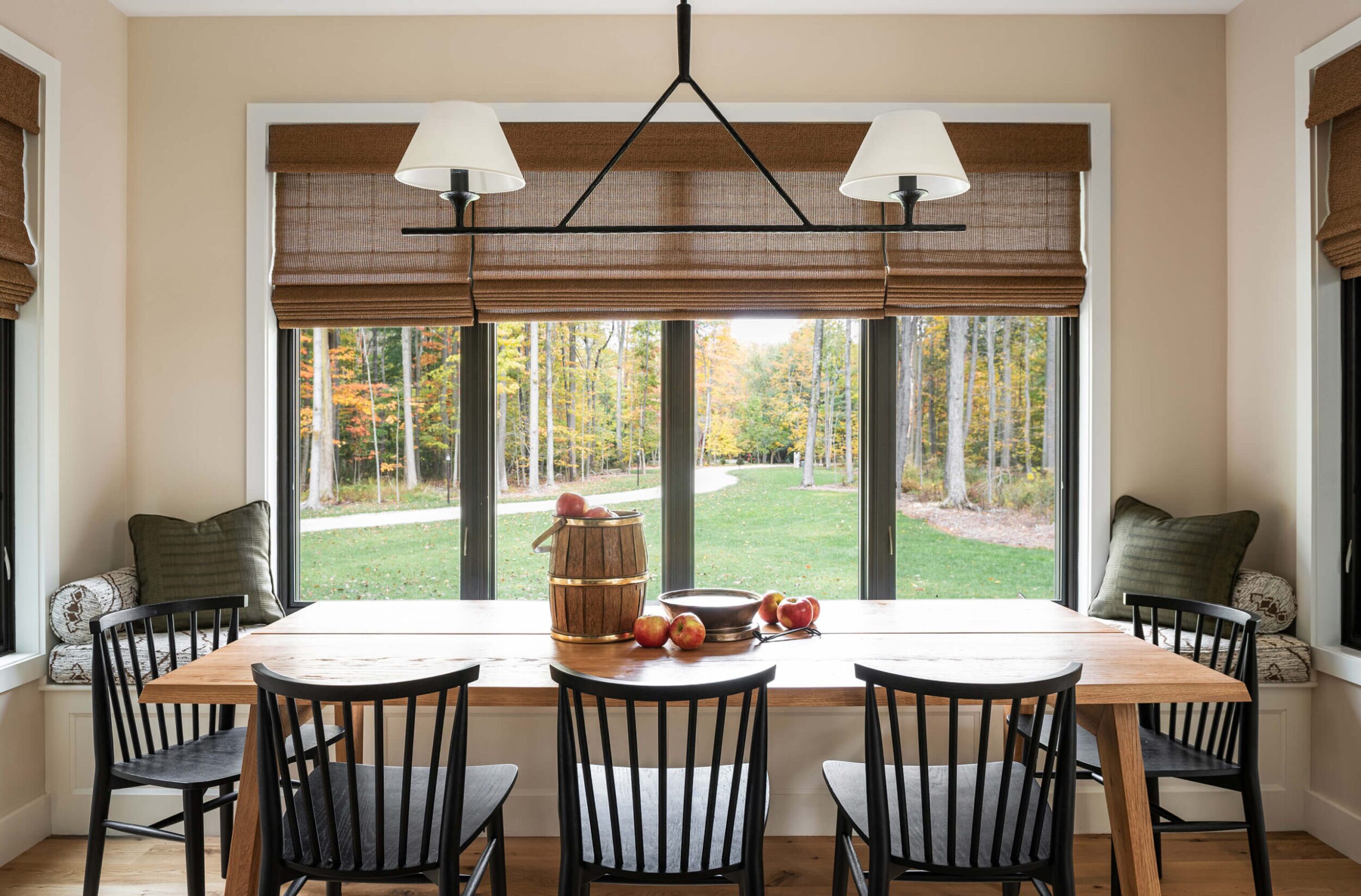 Cozy dining nook with wooden table, black chairs, large windows, and autumn forest view bringing natural light inside