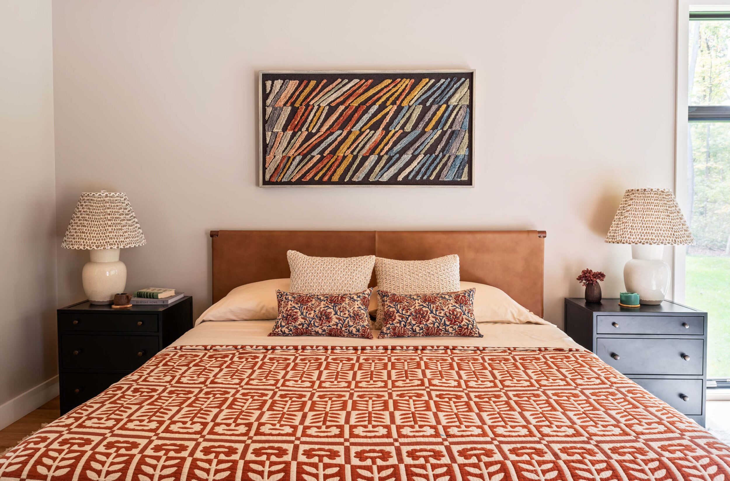 Bedroom with rust patterned bedspread, black nightstands, and abstract textile wall art