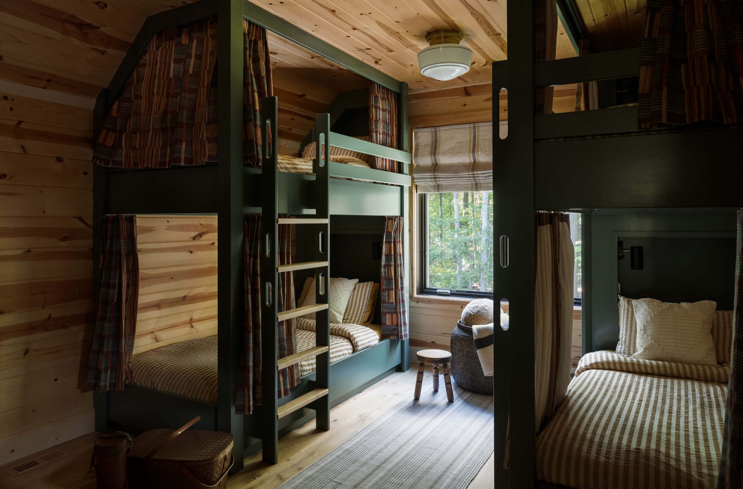Bunk-room nook with sage built-ins, twin beds with neutral striped bedding, botanical-print curtains, layered rugs, soft glow.