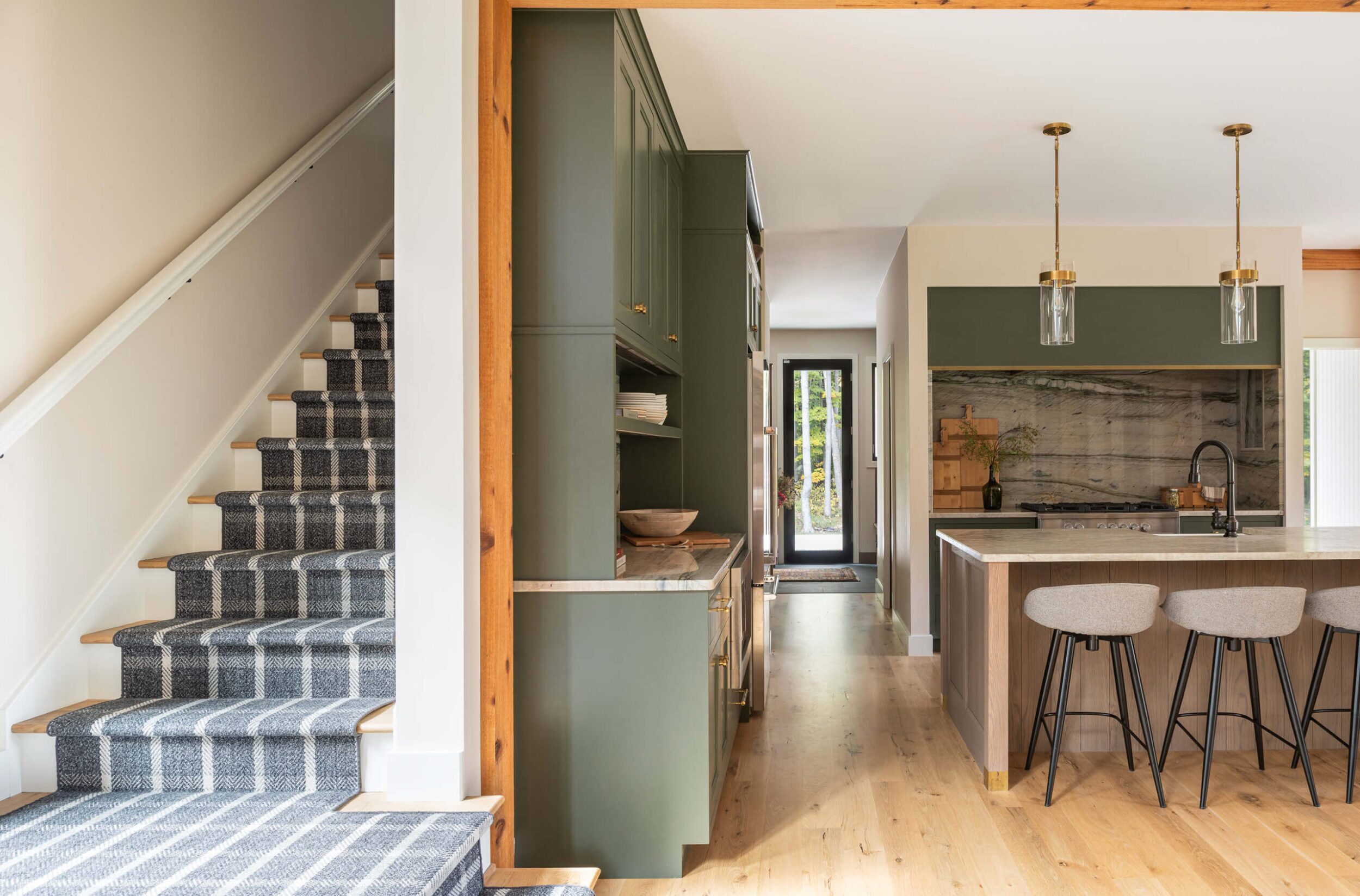 Open kitchen with green cabinetry, marble backsplash, and adjacent staircase with plaid runner