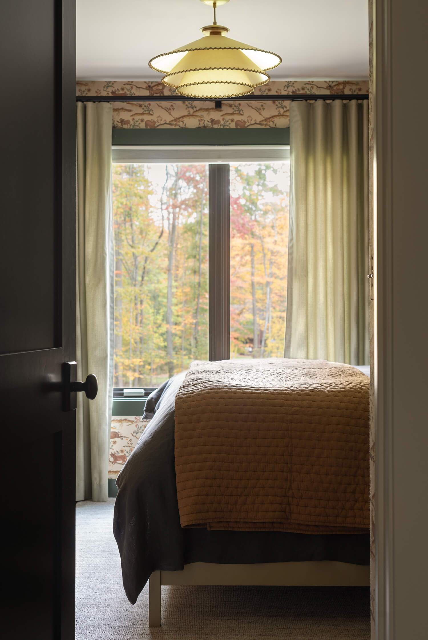 Cozy modern cabin bedroom with mustard quilt, large window, and forest view framed by soft curtains