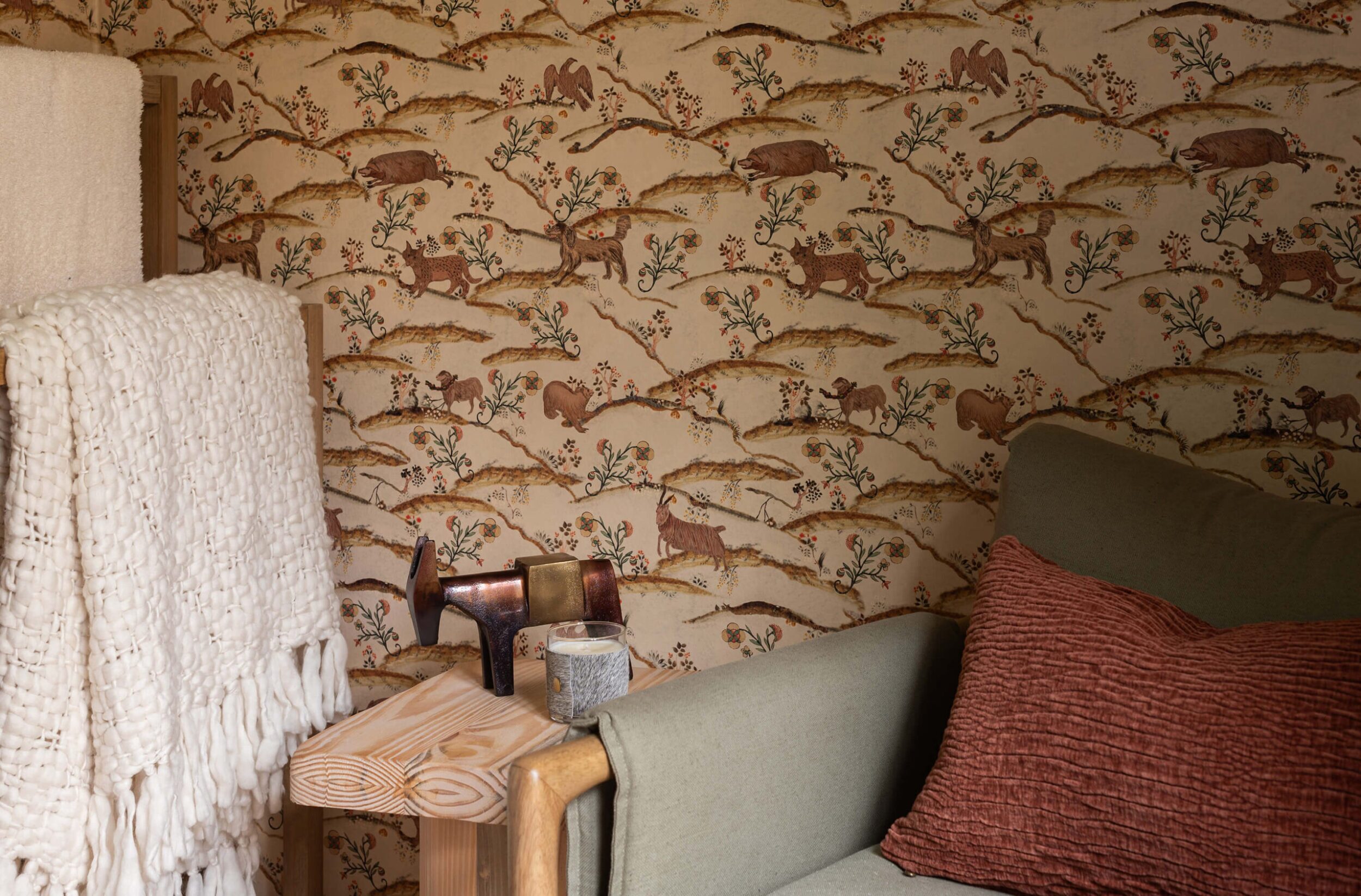 Cabin corner with earthy wallpaper, olive armchair, rust pillow, and wooden side table