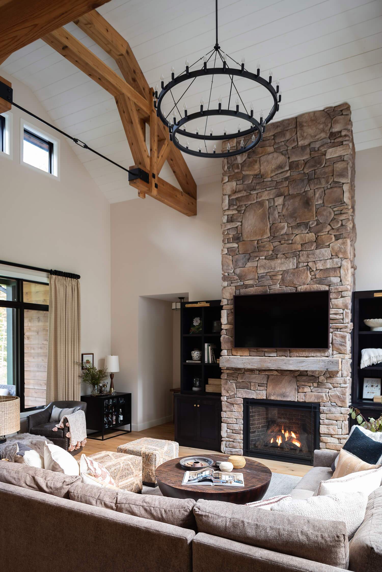 Living room with vaulted ceiling, stone fireplace, rustic chandelier, and cozy seating area with natural wood beams
