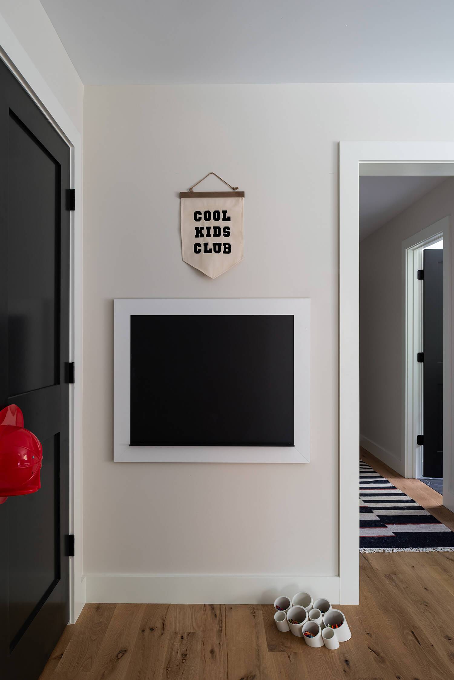 Wall with “COOL KIDS CLUB” banner and black chalkboard in children’s hallway play area with wooden floor.
