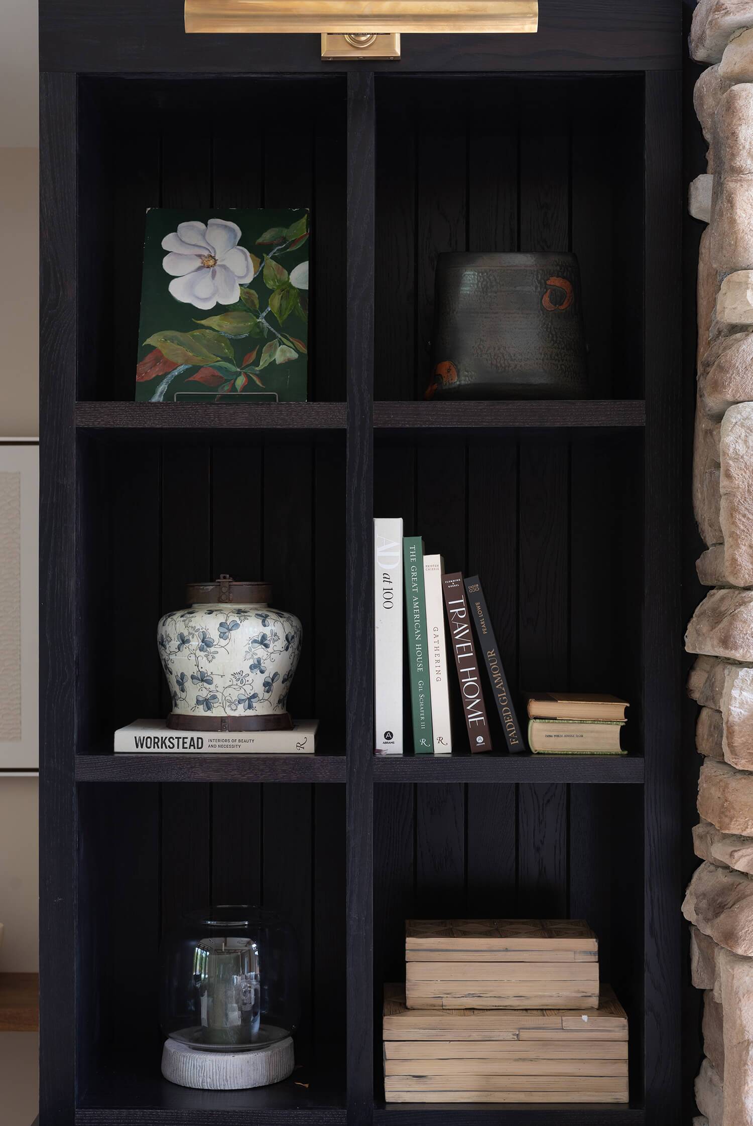 Built-in shelving next to stone fireplace with books, ceramic vase, framed artwork, and decorative accents in dark tones