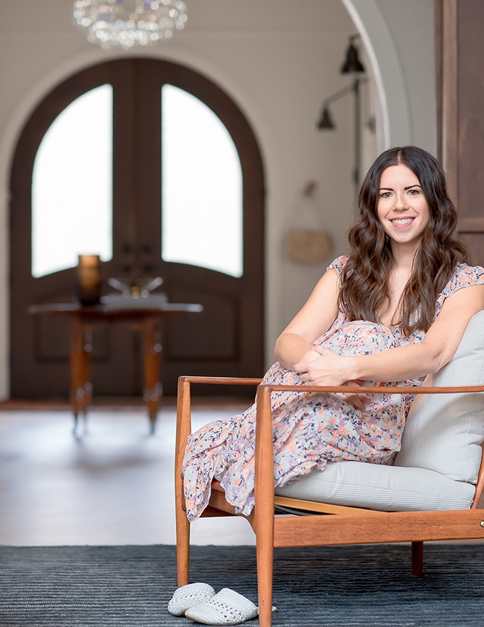 Woman in floral dress smiling while seated in modern chair, arched doorway and chandelier visible in background