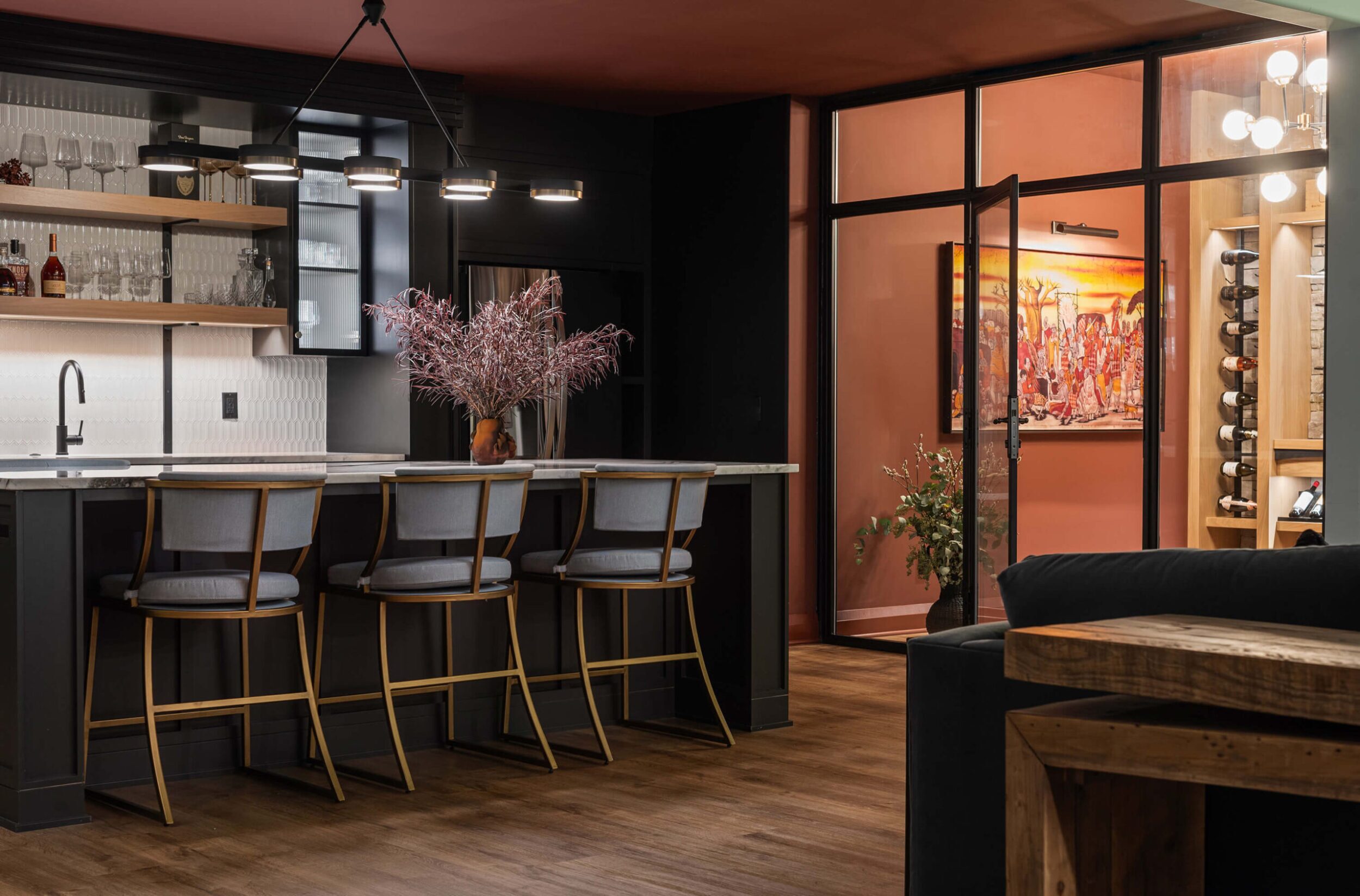Contemporary bar with marble countertop, cushioned stools, open shelves, and wine room visible through glass door