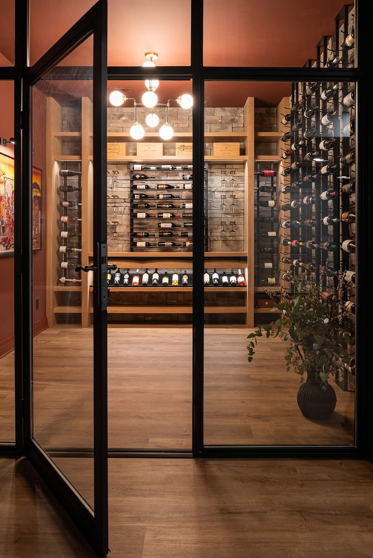Elegant wine cellar with wood racks, black metal bottle holders, stone accent wall, and chandelier lighting overhead
