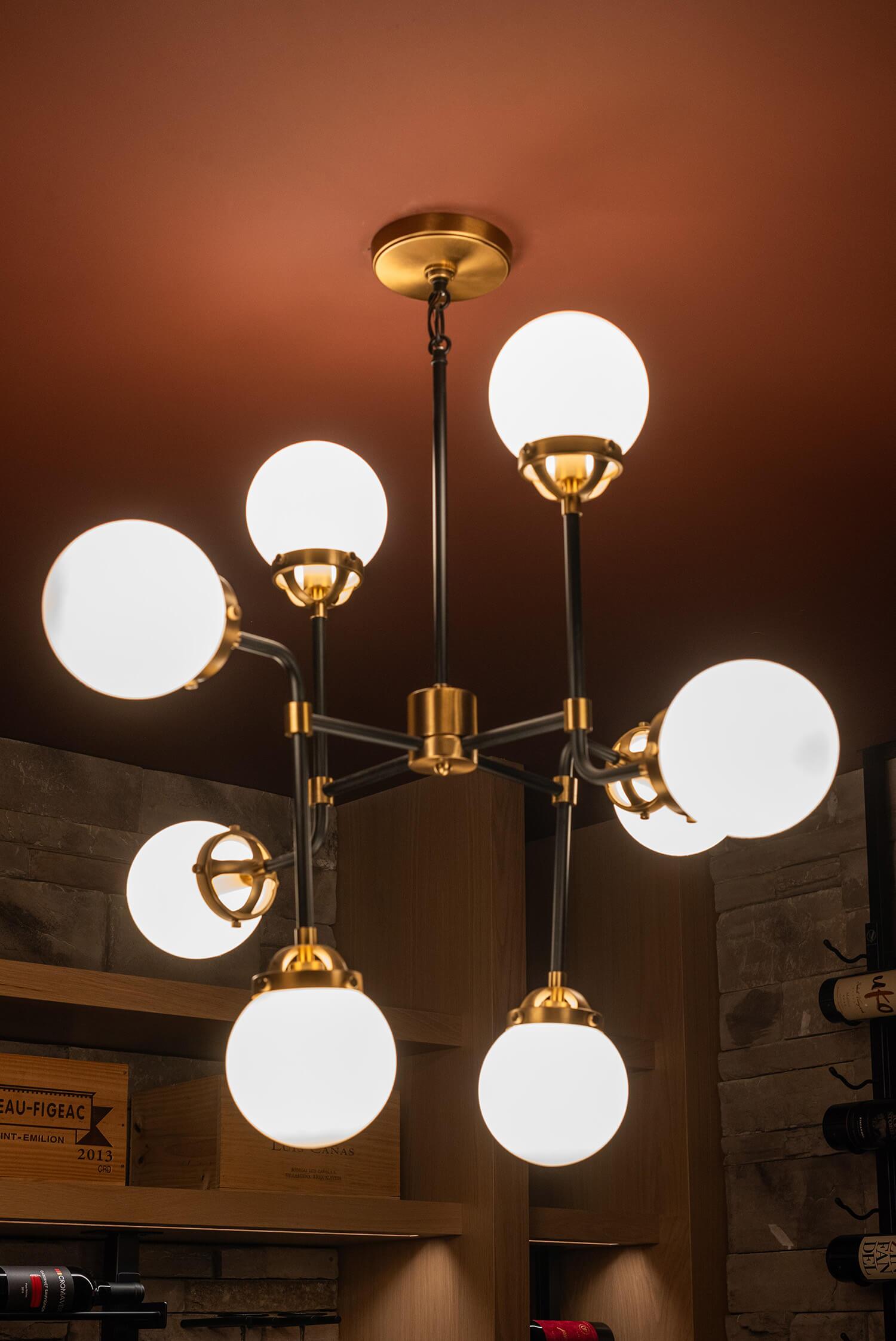 Contemporary chandelier with multiple globe lights, brass and black accents, set against warm ceiling and stone wine cellar