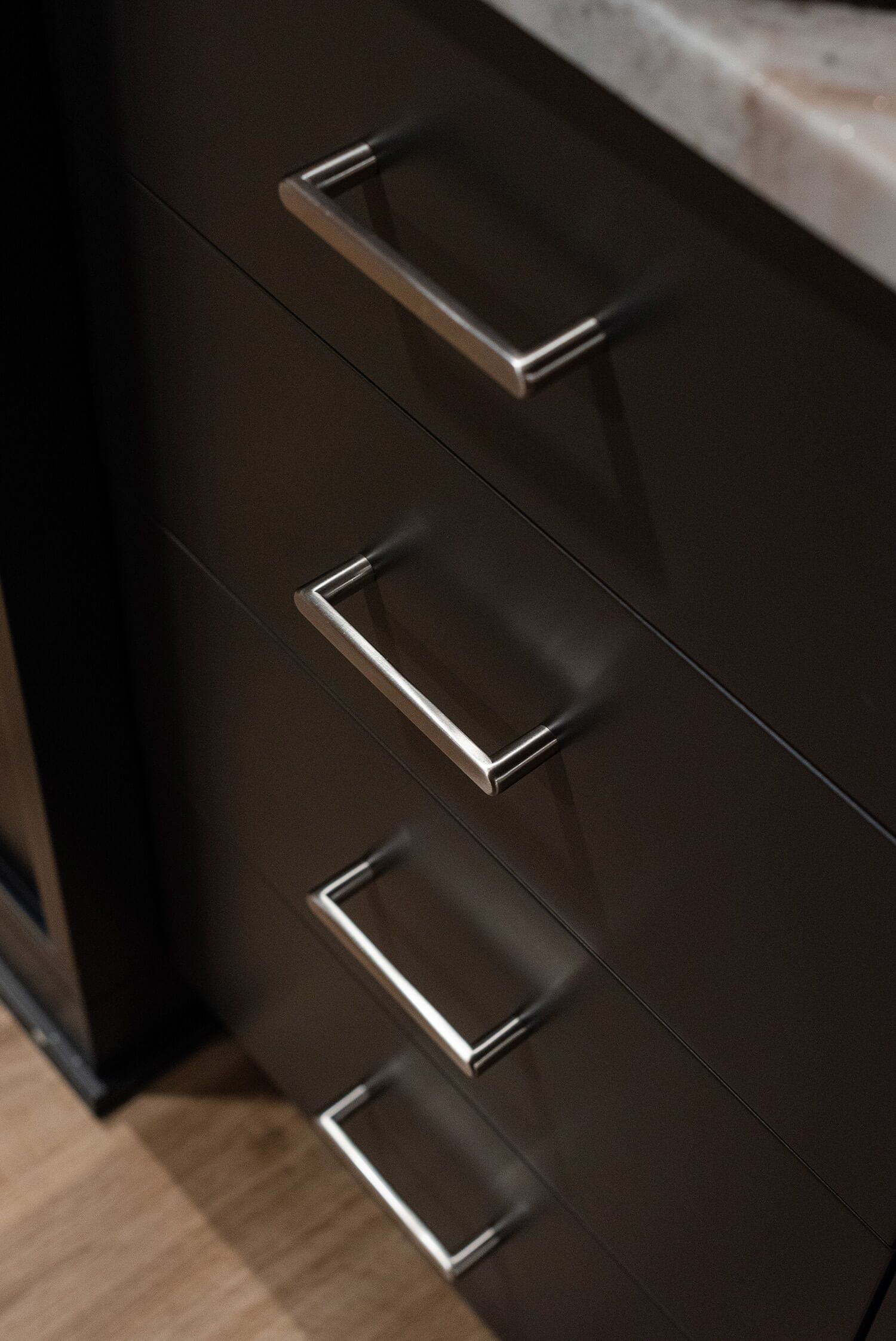 Close-up of sleek black drawers with brushed steel handles under marble countertop, modern cabinetry on hardwood flooring
