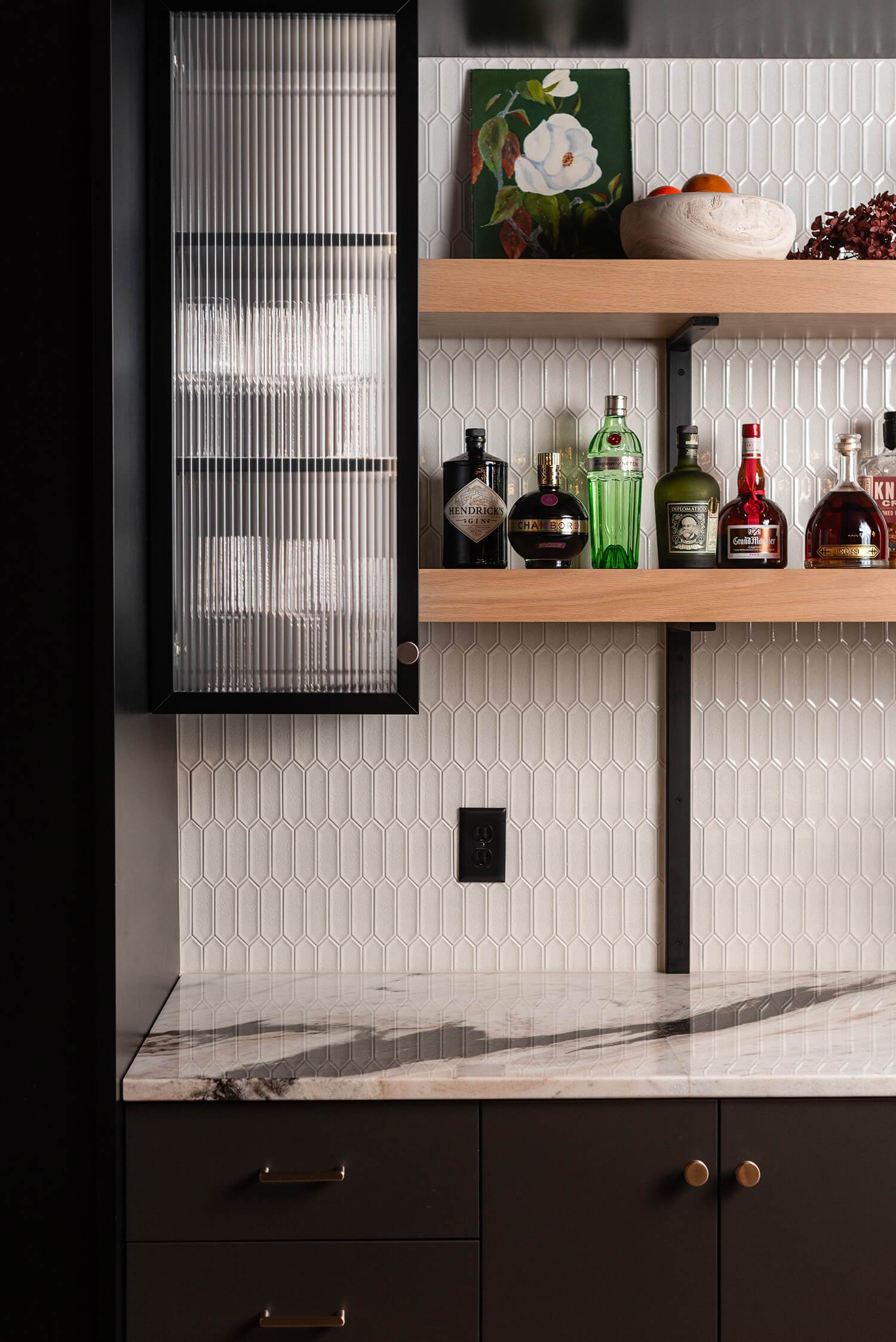 Bar cabinet with fluted glass door, wooden shelves holding liquor bottles, white hexagonal tile backsplash, modern design