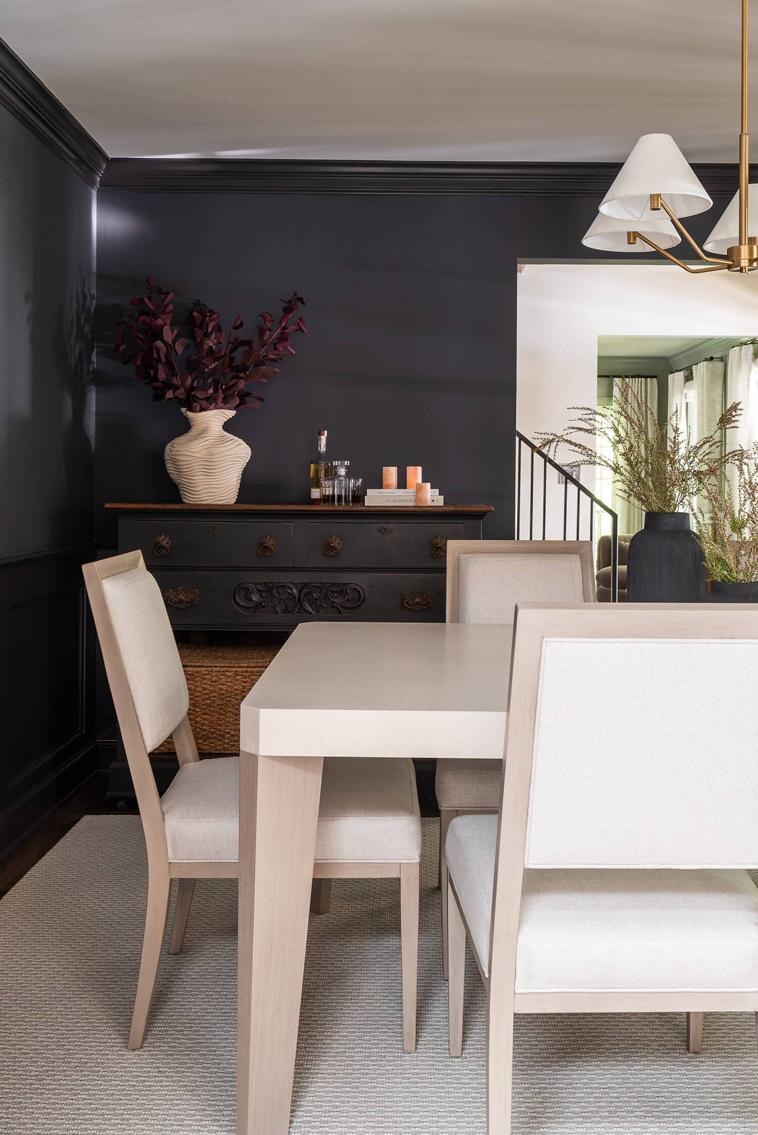 Dining room with light wood table, upholstered chairs, black sideboard, and dark painted walls.